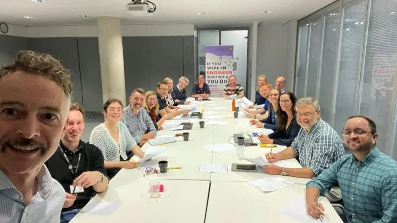 Group of people in a conference room sitting around a long table, smiling for the photo.