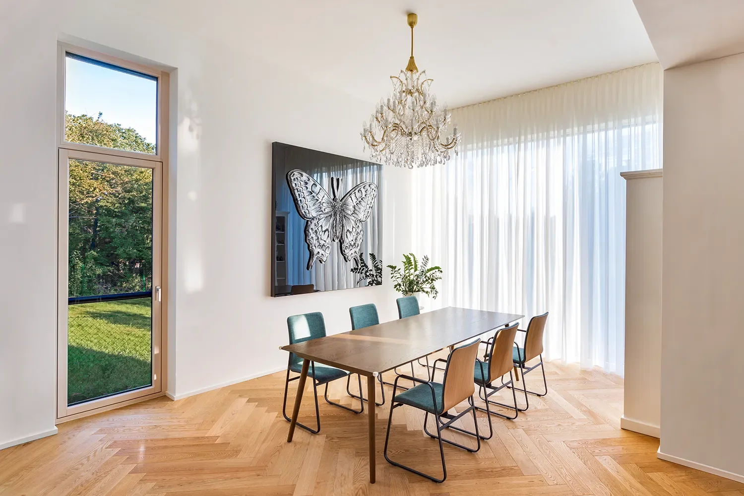 Helles Esszimmer mit Holzfußboden, einem großen Fenster, Vorhängen, einem Kronleuchter, einem Tisch mit sechs Stühlen und einer Wandkunst eines Schmetterlings.