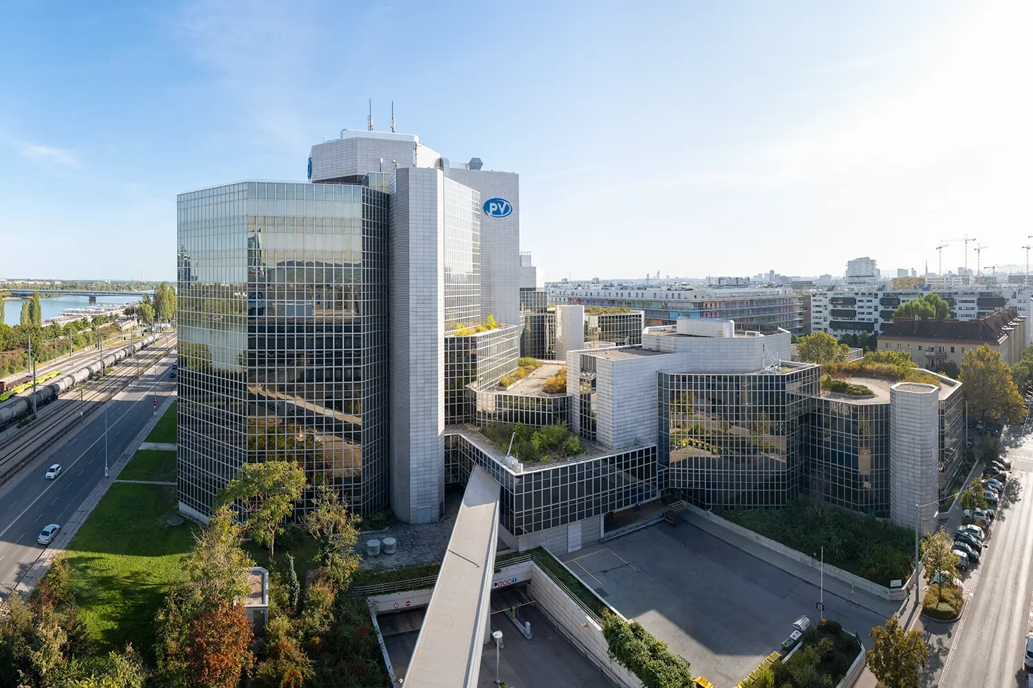 Moderne Bürogebäude mit Glasfassaden in einer städtischen Umgebung, Blick auf den Himmel, Straßen und Parkplätze im Vordergrund.