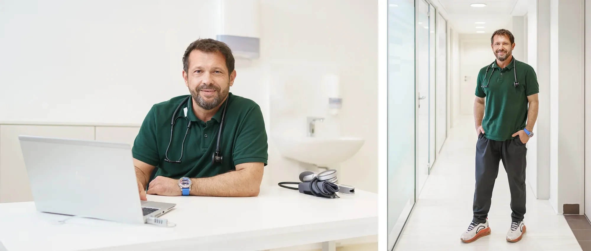 Ein männlicher Arzt in einem grünen Polo steht in einem Krankenhausflur, lächelt und hat die Hände in den Taschen.