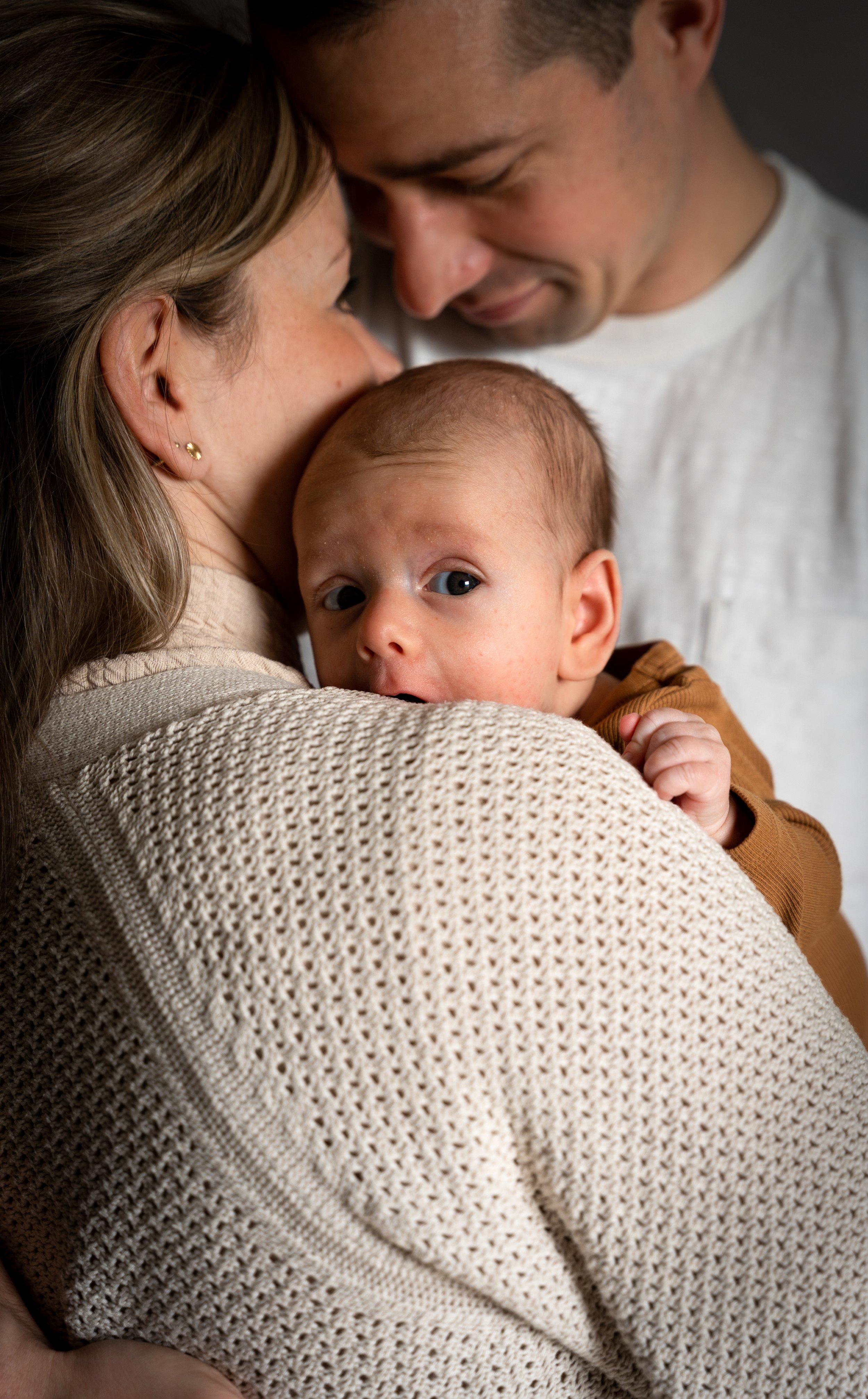 Close-up van een gezin met ouders en baby die knuffelen en gezichten dicht bij elkaar brengen.