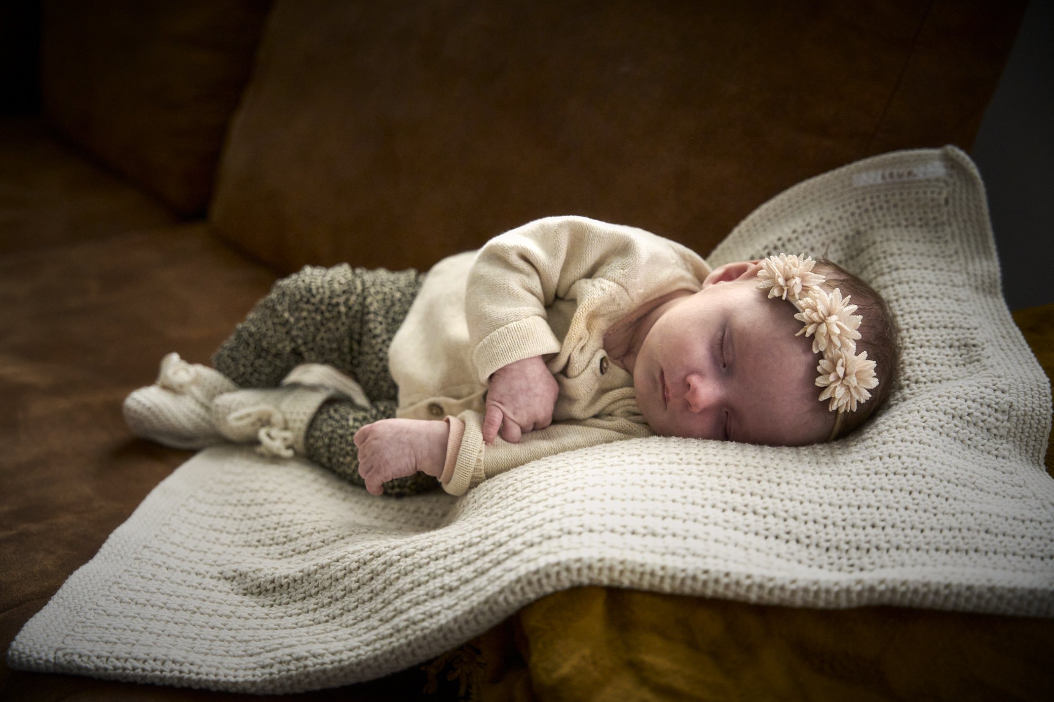 Een slapende baby met een bloemenkroon op haar hoofd ligt op een afdrukbare lappendeken.