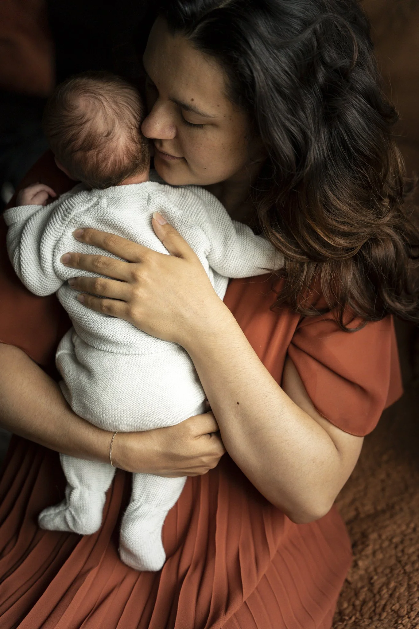 Een vrouw houdt een pasgeboren baby dicht tegen zich aan, beiden glimlachen en lijken te genieten van een intiem moment.
