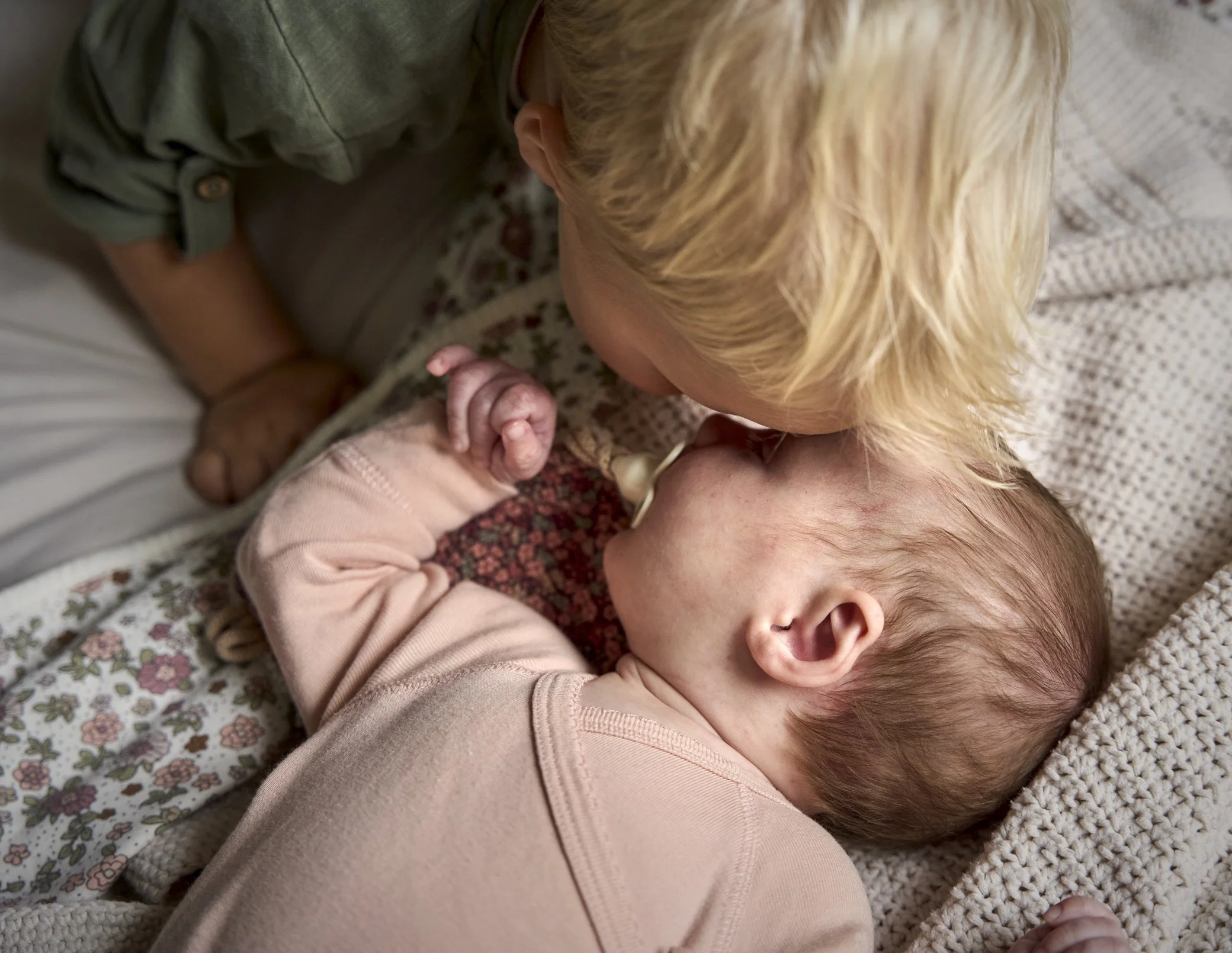 Dochter kust haar babyzusje op het voorhoofd terwijl deze ligt in bed.