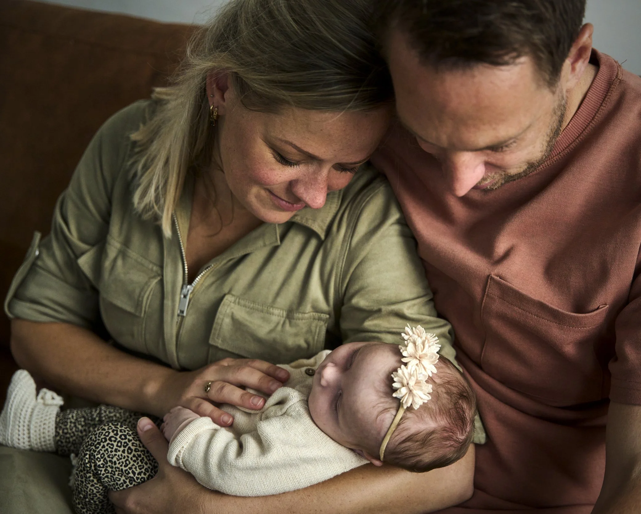 Een vrouw houdt een pasgeboren baby vast terwijl een man en een vrouw dichtbij de baby staan, alle drie glimlachend en liefdevol.