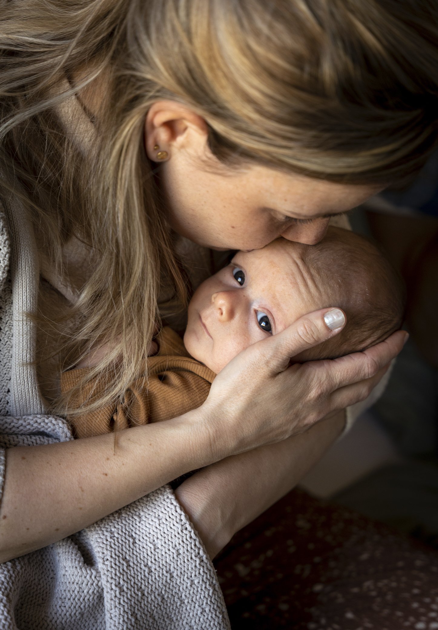 Een vrouw die haar hoofd neerlegt op de hoofd van een baby die haar aankijkt. Unieke lifestyle newborn shoot in Terheijden
