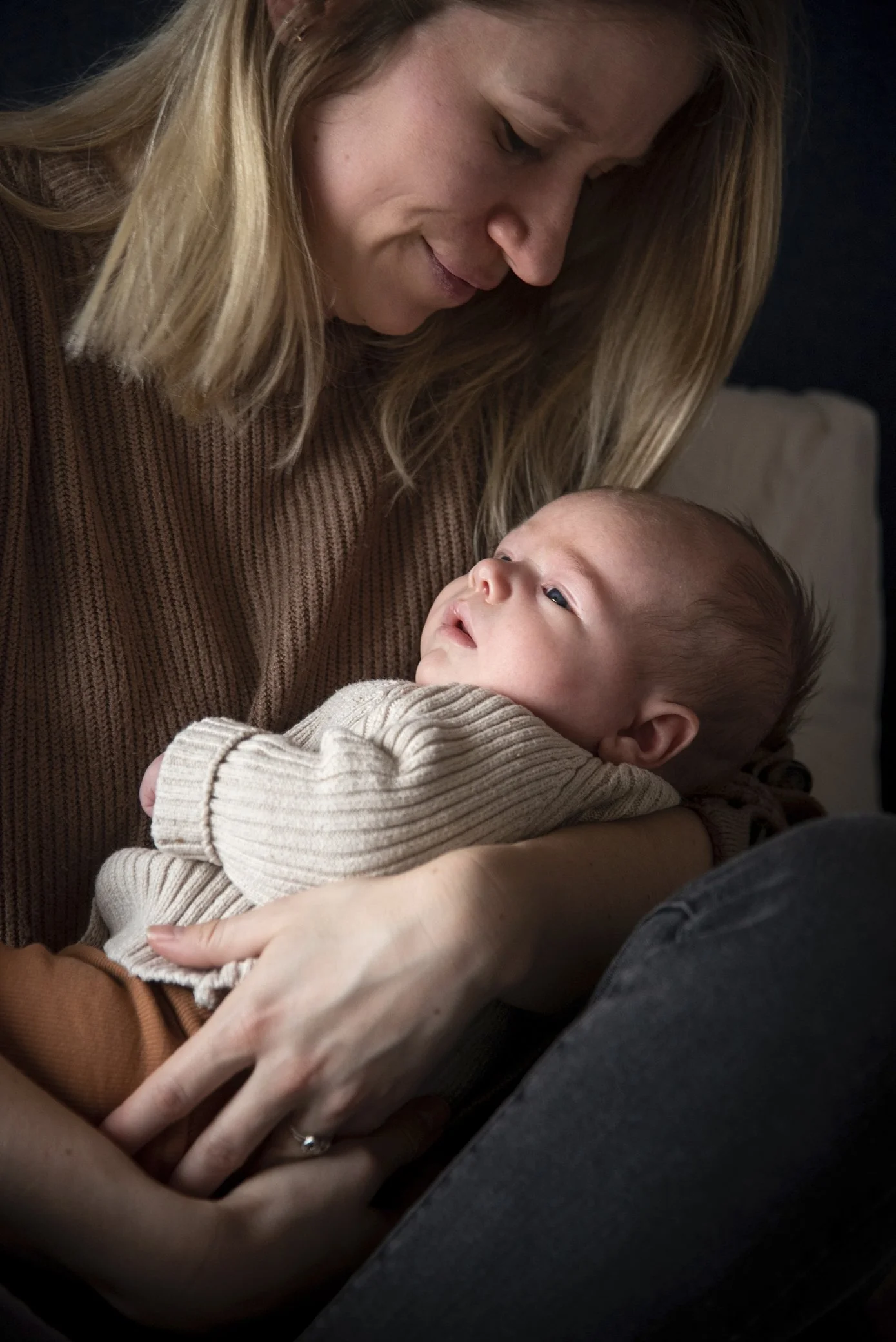 Een vrouw houdt een baby in haar armen terwijl ze samen naar elkaar kijken, binnen een rustige sfeer.