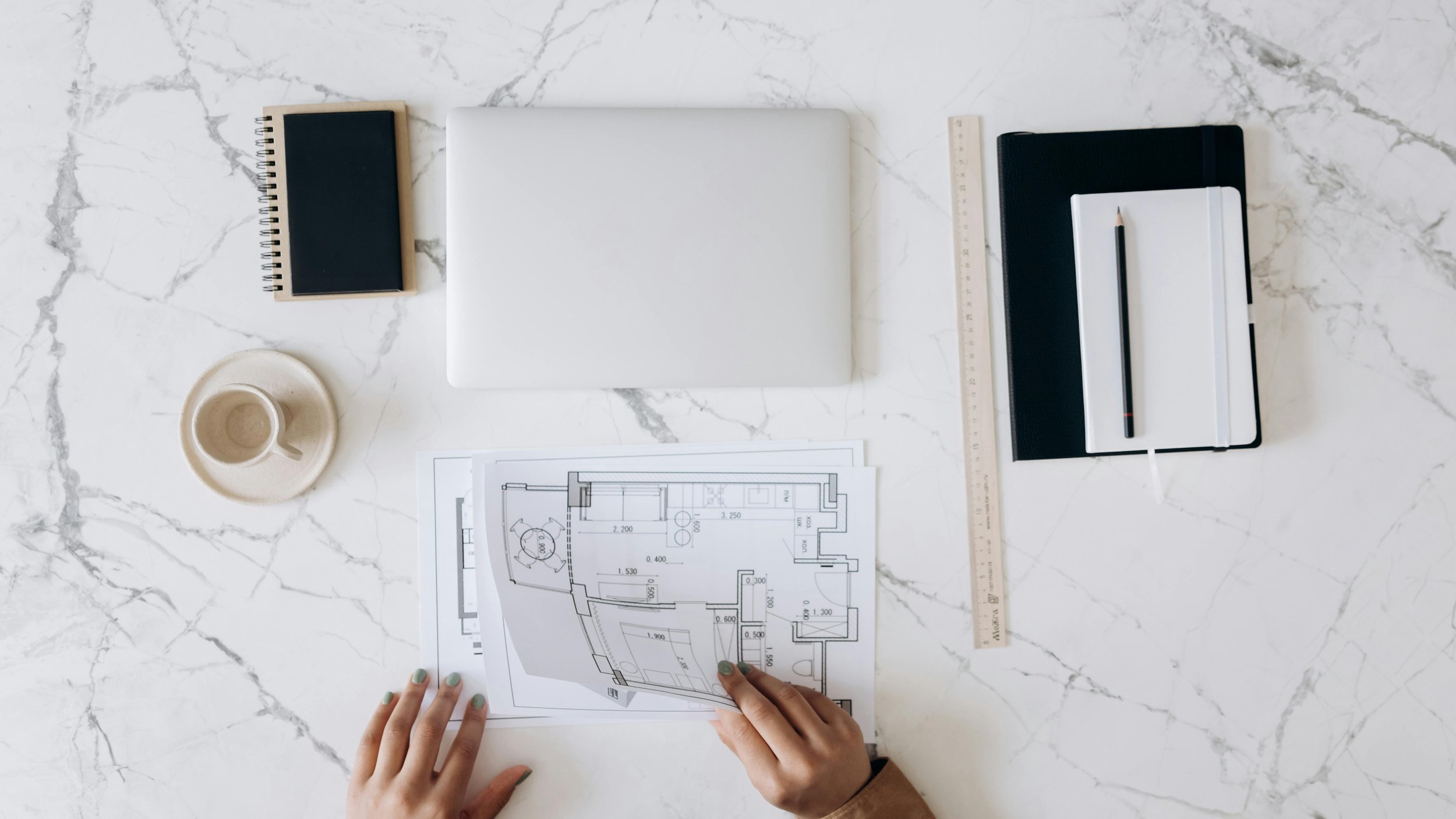 Technical drawing on a desk beside a laptop, notebook and ruler