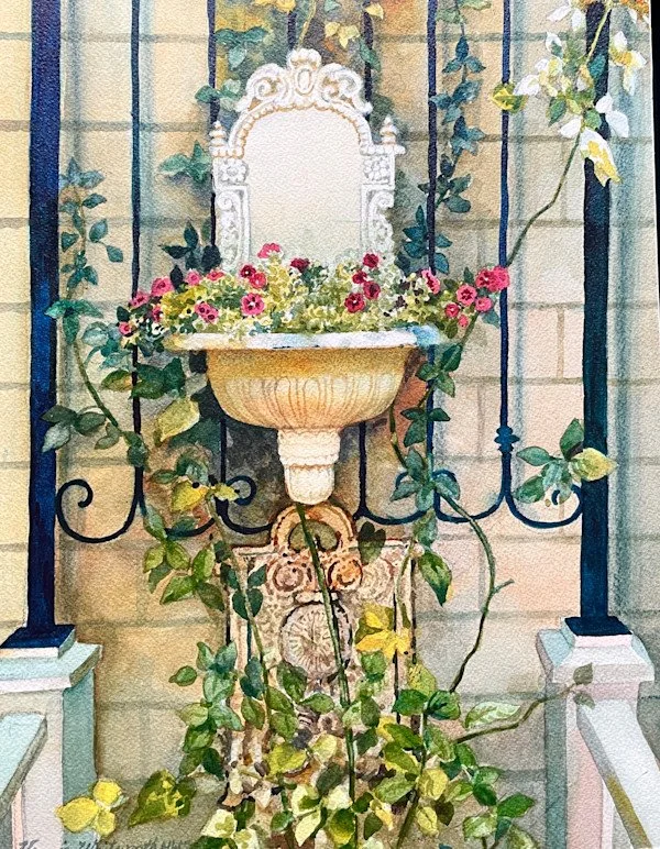 Decorative garden fountain with pink flowers, surrounded by ivy on a black iron fence with brick wall background.
