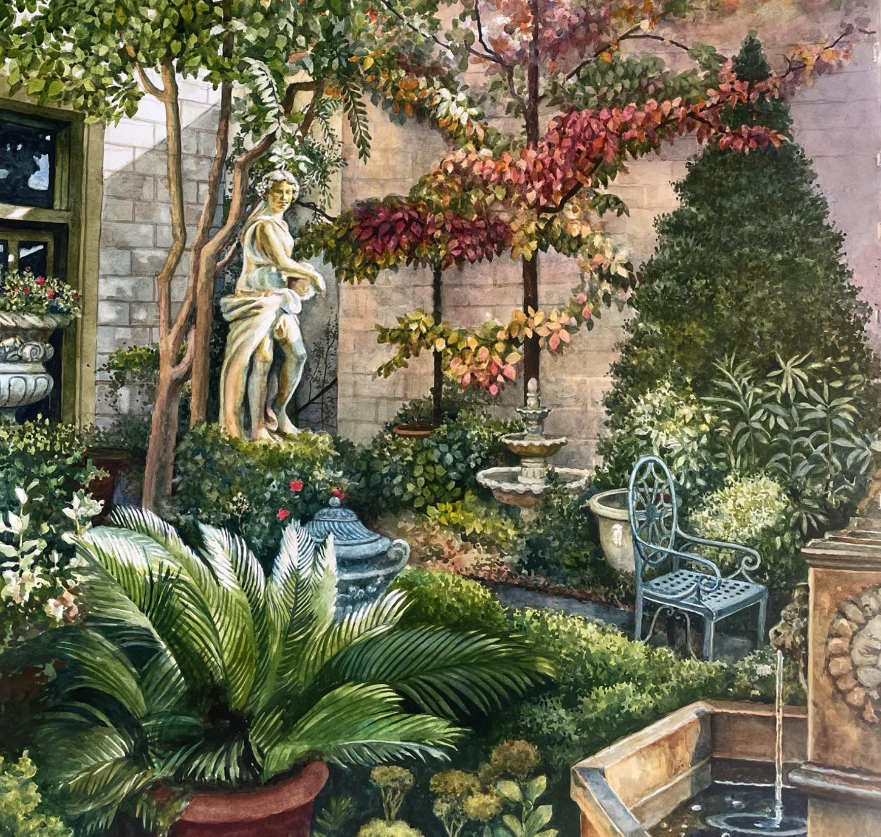 A lush garden corner with green plants, bushes, a fountain, a vintage metal chair, and a statue of a woman near a stone wall and tree with colorful leaves.