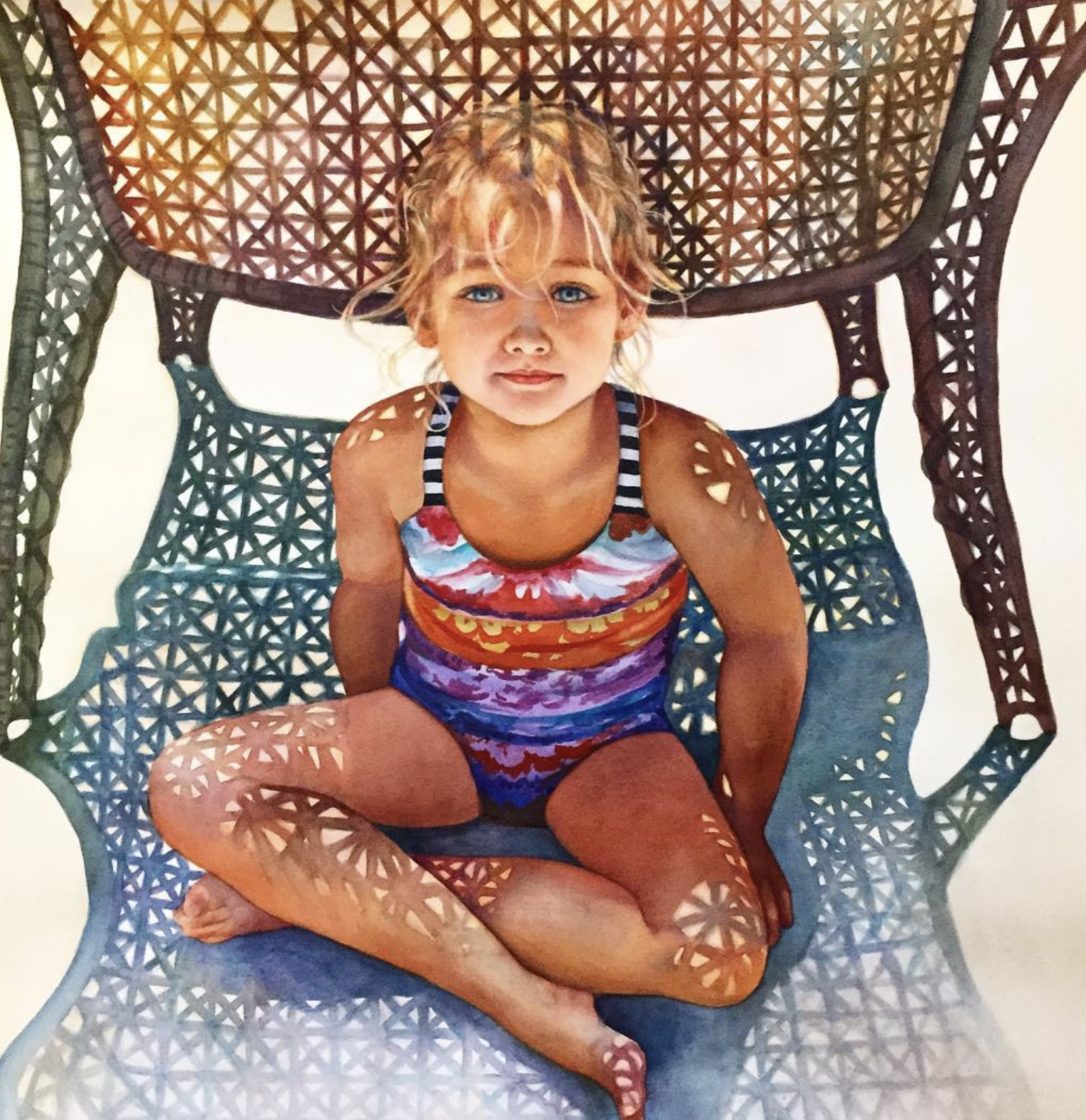A young girl with curly blonde hair and blue eyes sitting cross-legged in a decorative brown wicker chair with a circular pattern. She is wearing a colorful striped sleeveless top and matching shorts, smiling slightly, looking at the camera, with sun