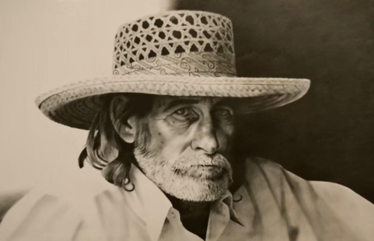 Black and white photograph of an older man with a serious expression, wearing a wide straw hat and a collared shirt.