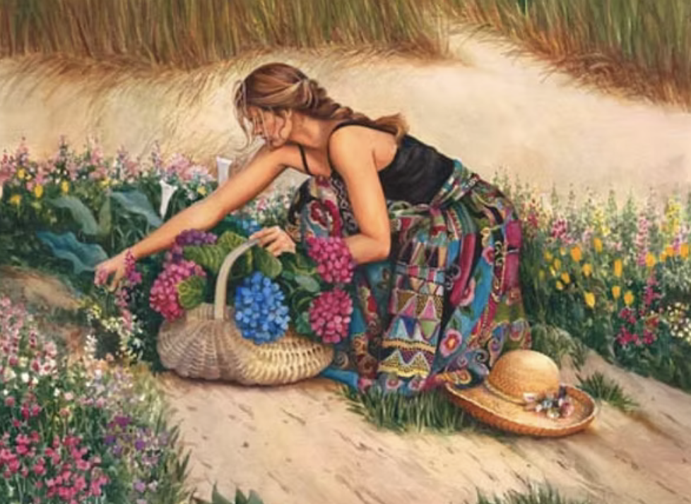 A woman with long brown hair in a braid, wearing a black top and colorful patchwork skirt, is kneeling on a dirt path surrounded by wildflowers, with a straw hat and a woven basket filled with purple and pink hydrangeas nearby.