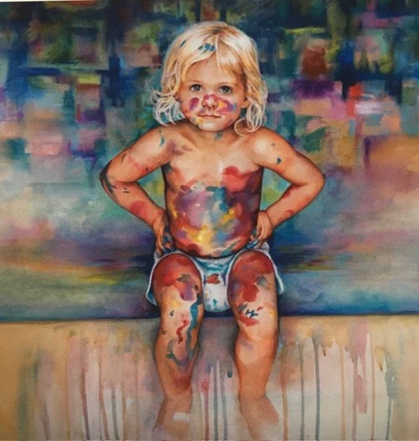 A young child with blonde hair sitting on a ledge covered in colorful paint.