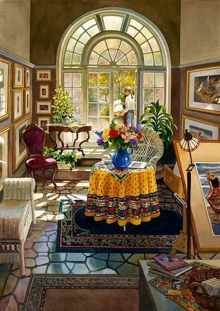 Interior of an art studio or gallery with a large arched window, a table with a colorful tablecloth and a vase of flowers, artwork on the walls, and a woman standing near the window.