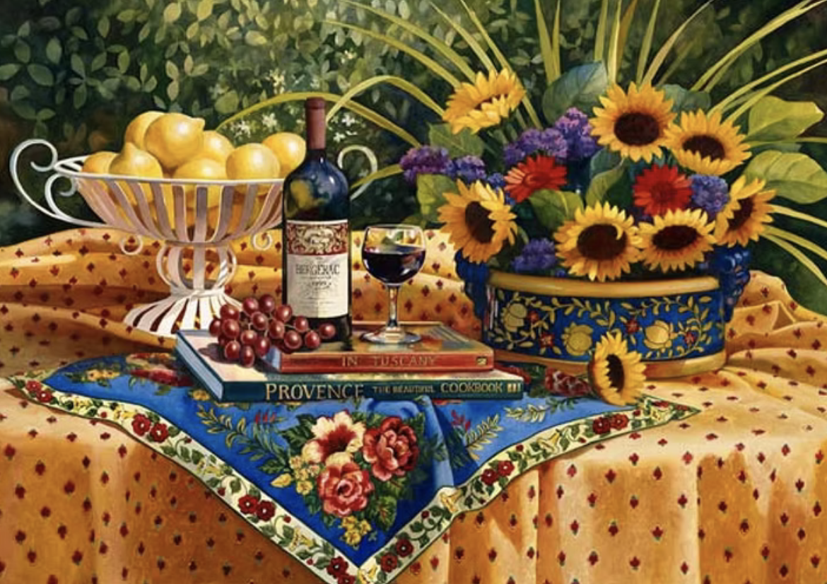 Colorful still life with a basket of lemons, a bunch of grapes, a bottle of red wine with a glass, and a vase of sunflowers and other flowers on a table with patterned cloth and books.