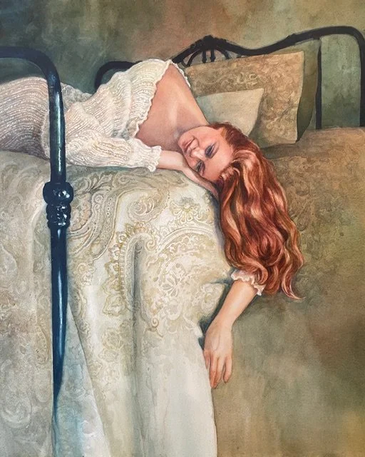 A woman with long red hair in a white sweater is lying on a bed with an ornate blanket, resting her head on a pillow with a floral design, smiling with her eyes closed.