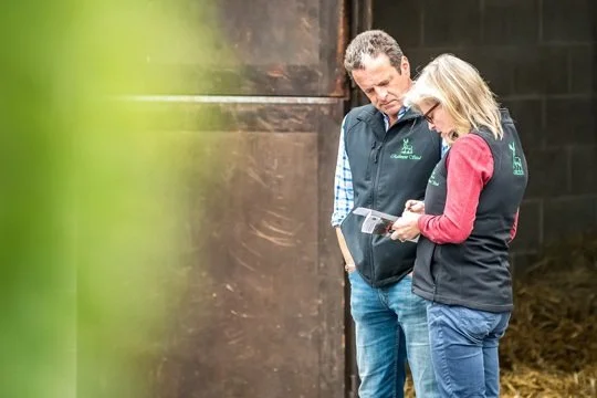 Peter Molony and Sarah Molony from Rathmore Stud, Limerick standing next to a barn, looking at a tablet together.
