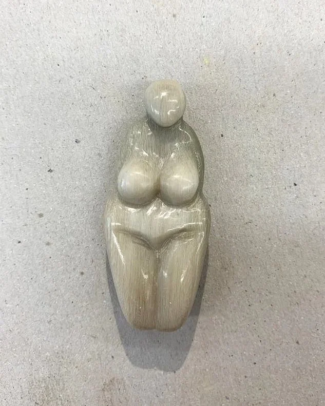 Sculpture of a woman with rounded hips and thighs, made of smooth, shiny material, mounted on a light-colored wall.