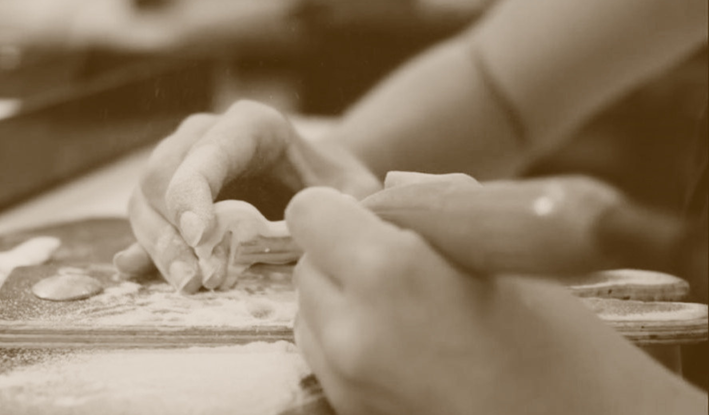 Close-up of two children's hands playing with clay or dough on a table, with some small objects and flour scattered around.