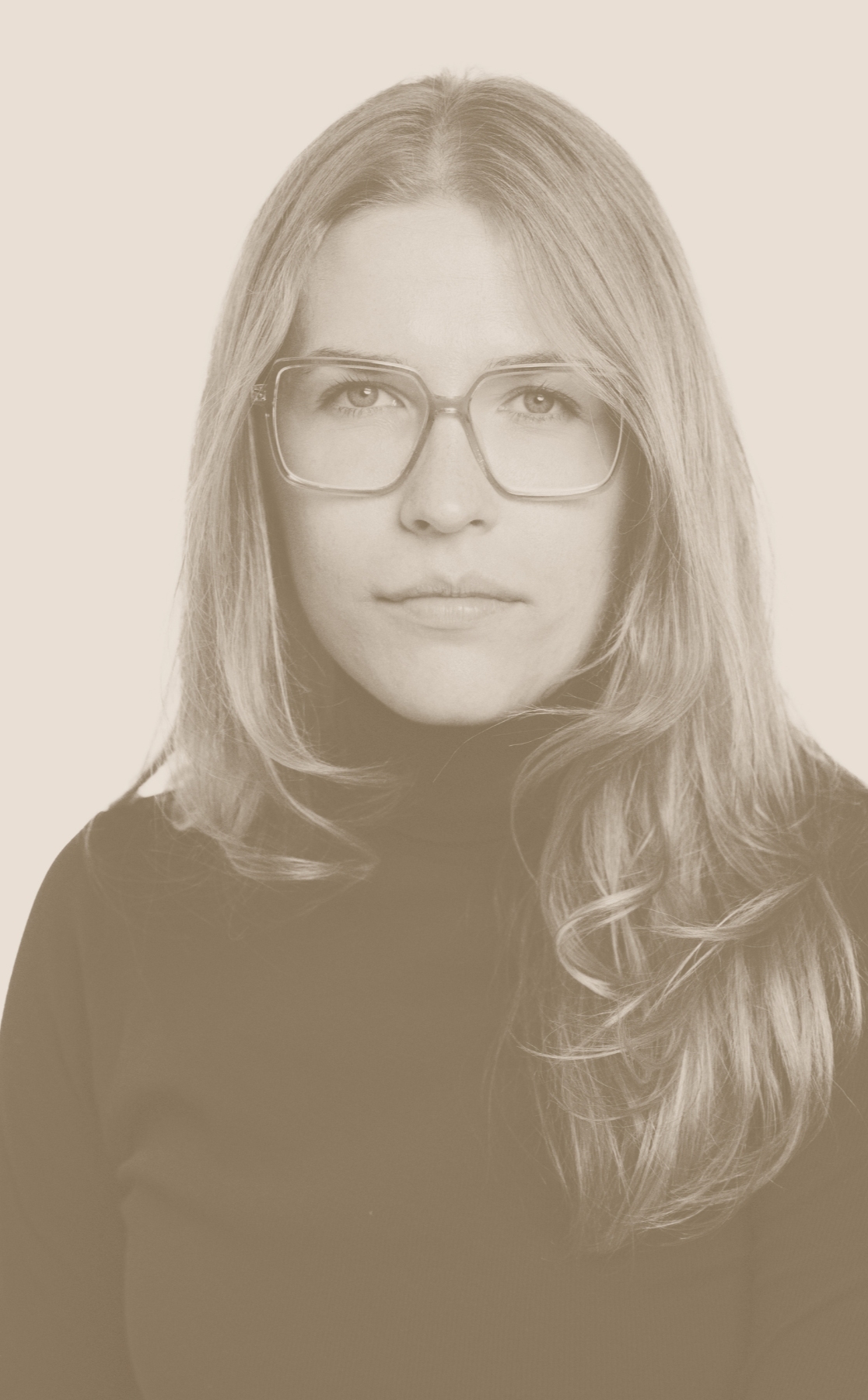 A portrait of a woman with shoulder-length wavy hair wearing large rectangular glasses and a black turtleneck, looking directly at the camera.