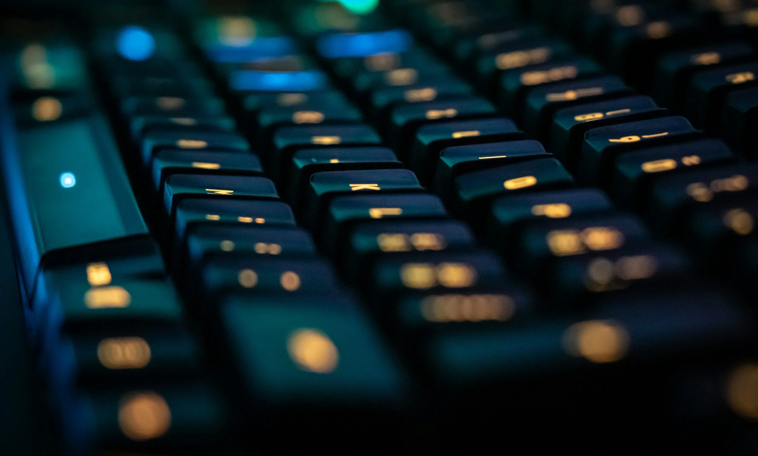 Blick auf eine Computertastatur mit blauer Beleuchtung, Fokus auf die Tasten im mittleren Bereich, unscharfer Hintergrund.
