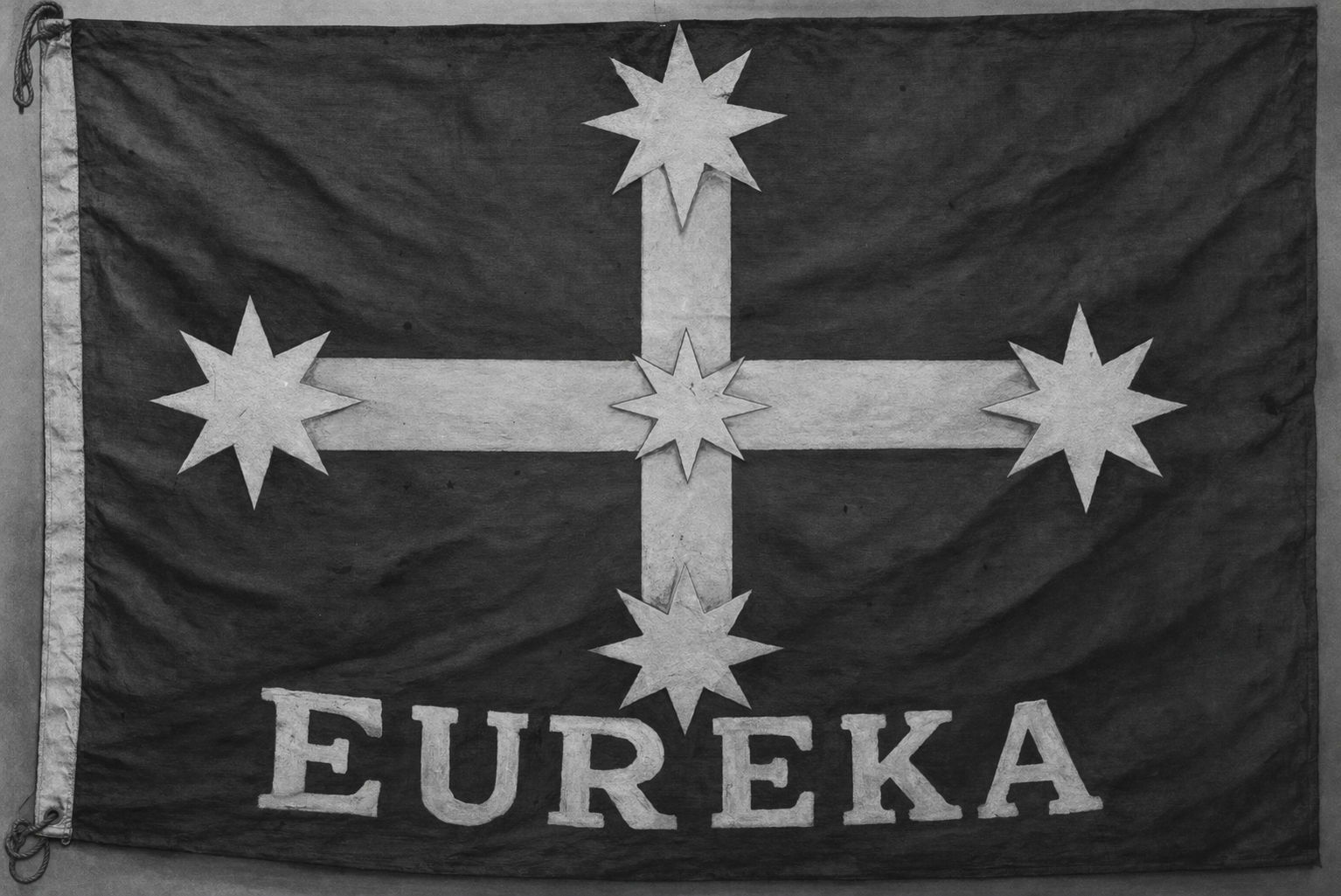 A black and white flag with a white cross and five six-pointed stars, and the word "EUREKA" written at the bottom.