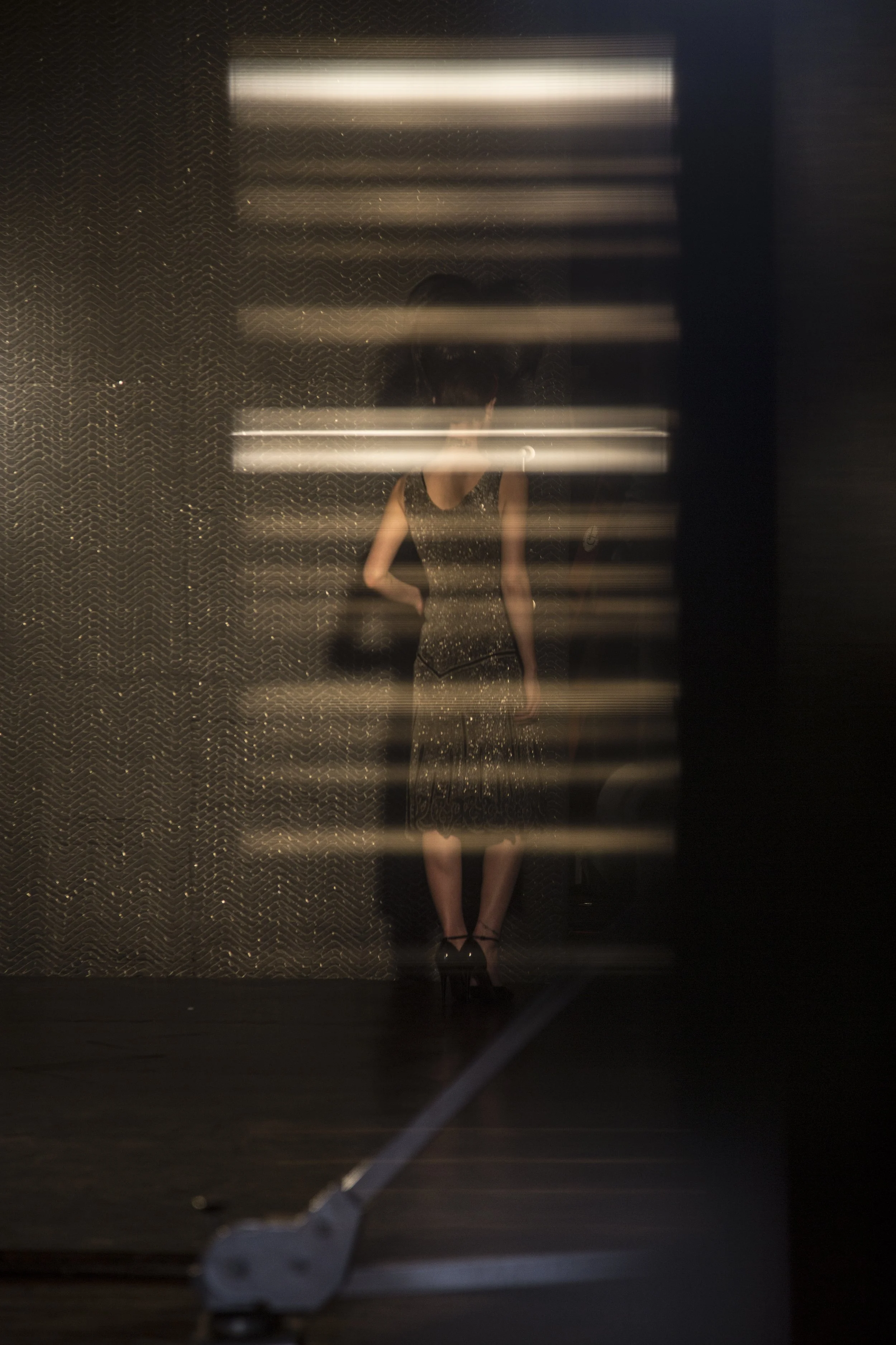 Reflet d'une femme portant une robe noire à paillettes, vu à travers une surface avec des lignes de lumière, créant un effet de reflet flou.