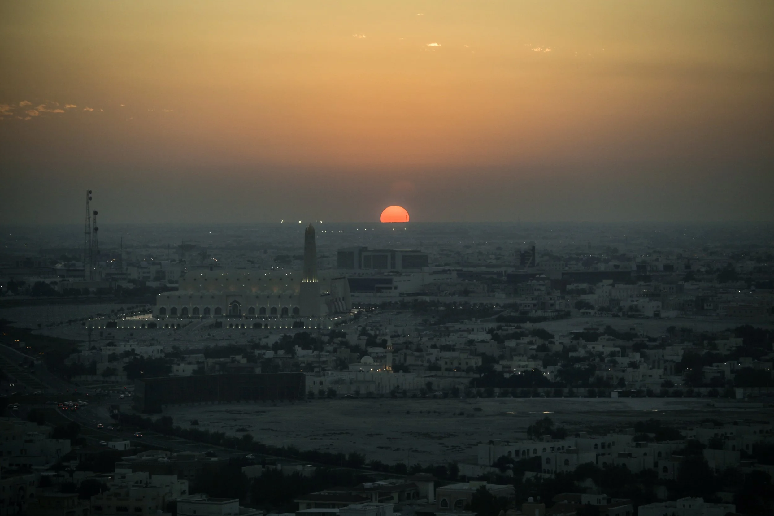 Coucher de soleil sur une ville avec des bâtiments modernes et un minaret en avant-plan.