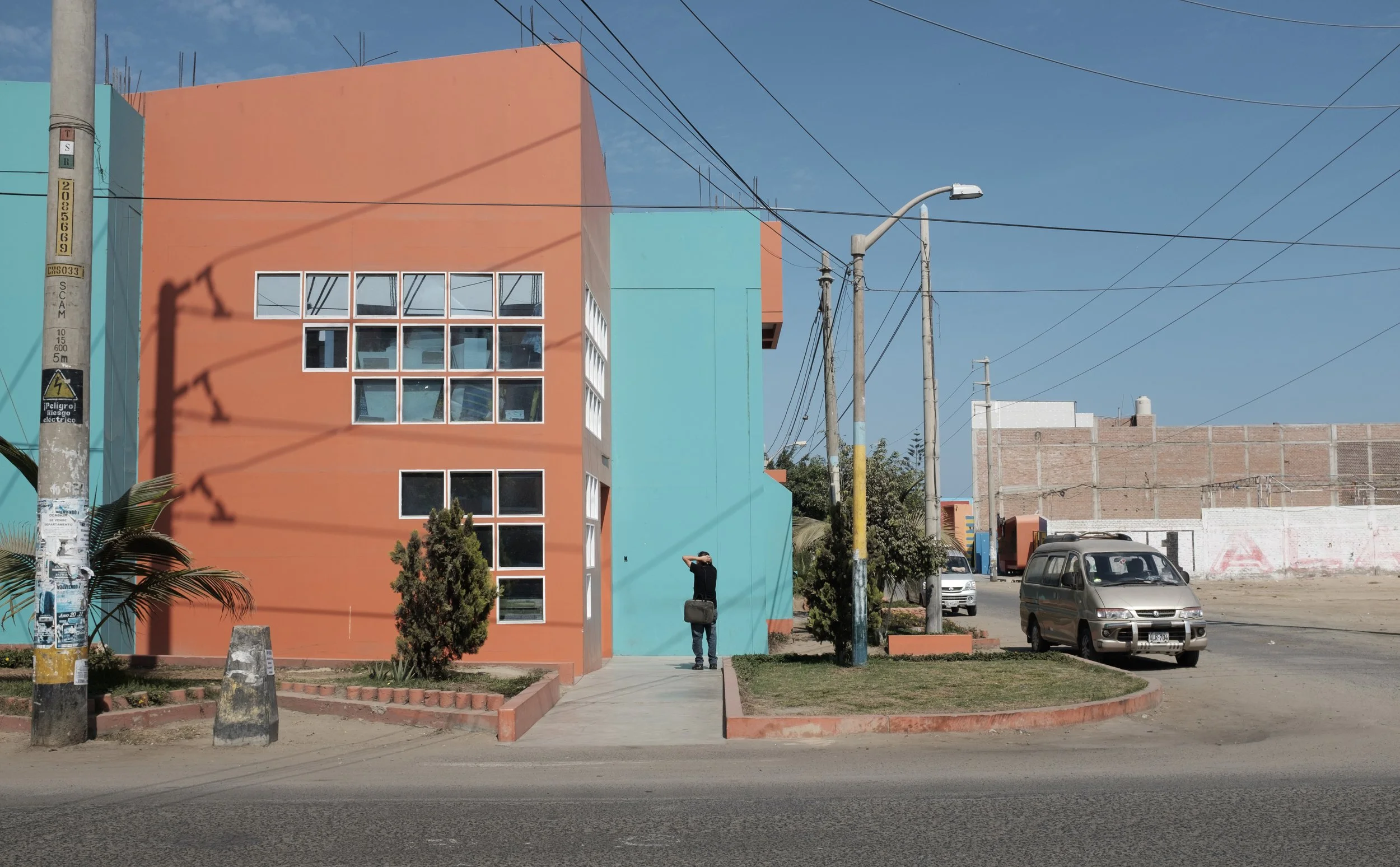 Bâtiment coloré avec des fenêtres blanches, arbres et lampadaires dans une rue ensoleillée.