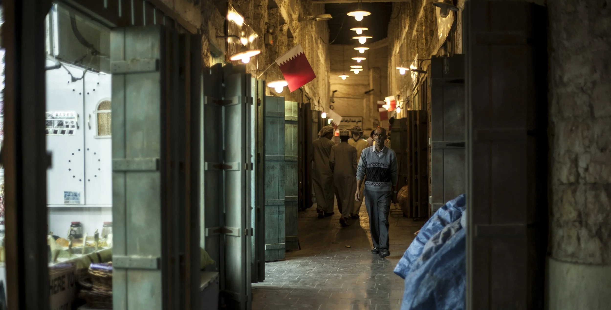 Vue de vue montrant une allée couverte dans un marché, avec des hommes habillés en vêtements traditionnels, certains portant des couvre-chefs, et des lampes suspendues au plafond.