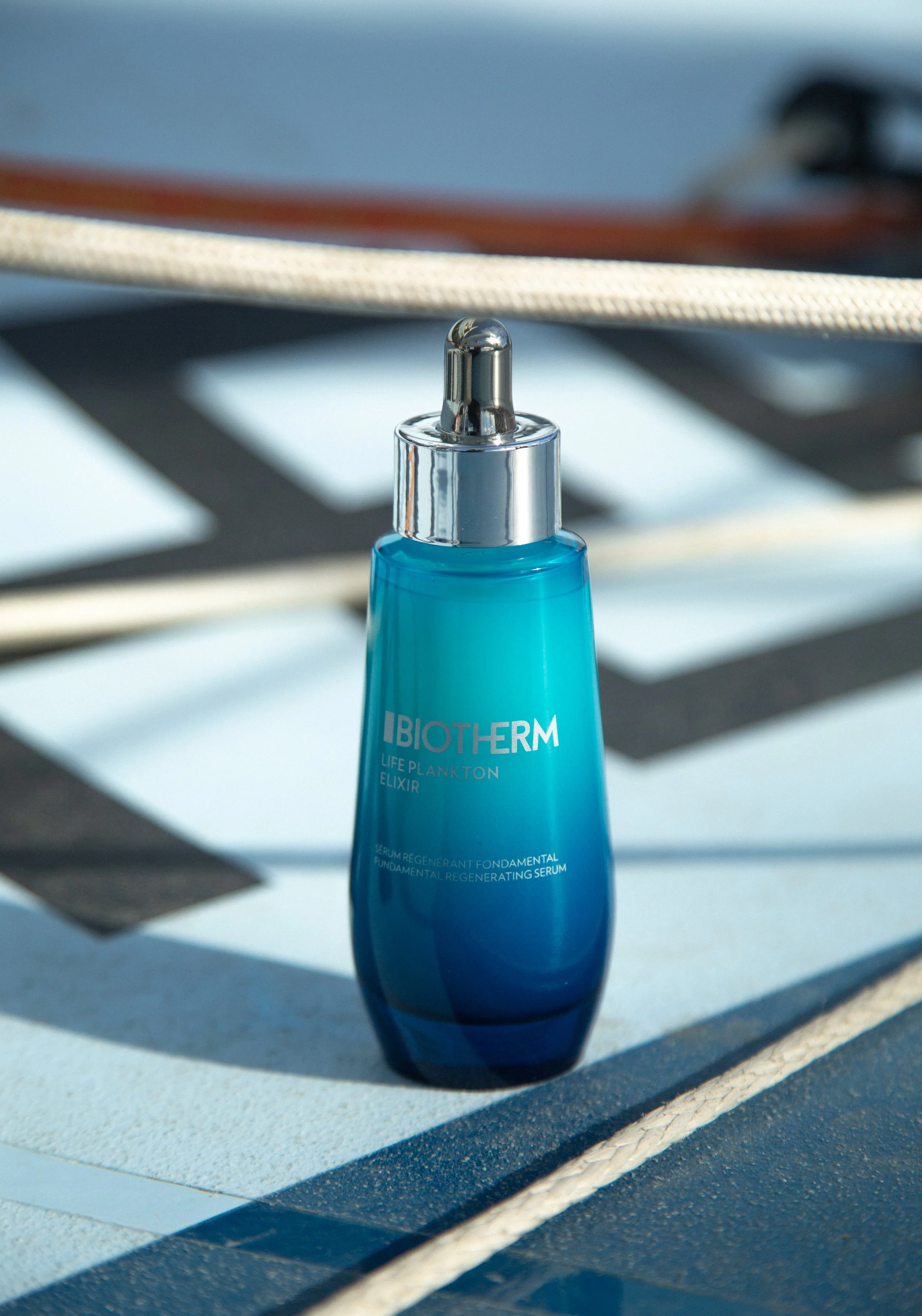 Flacon bleu de sérum biotherm Life Plankton, placé sur une surface blanche avec des ombres et rayures visibles autour.