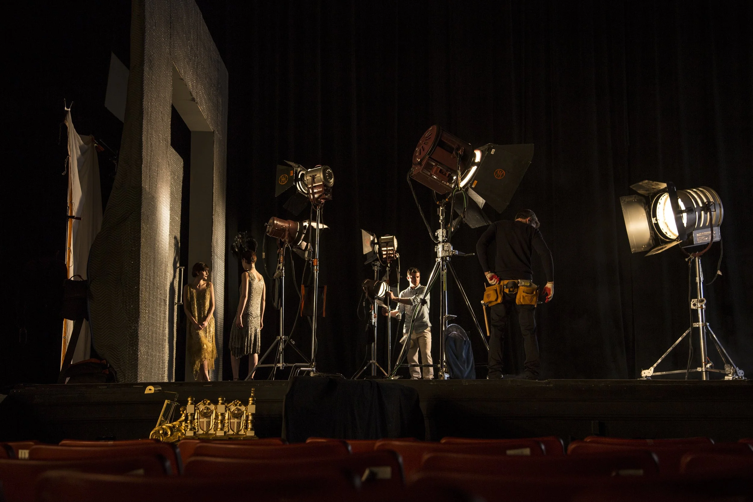Une scène de tournage avec des caméras, des éclairages et deux mannequins en robes dorées sur une scène de théâtre.