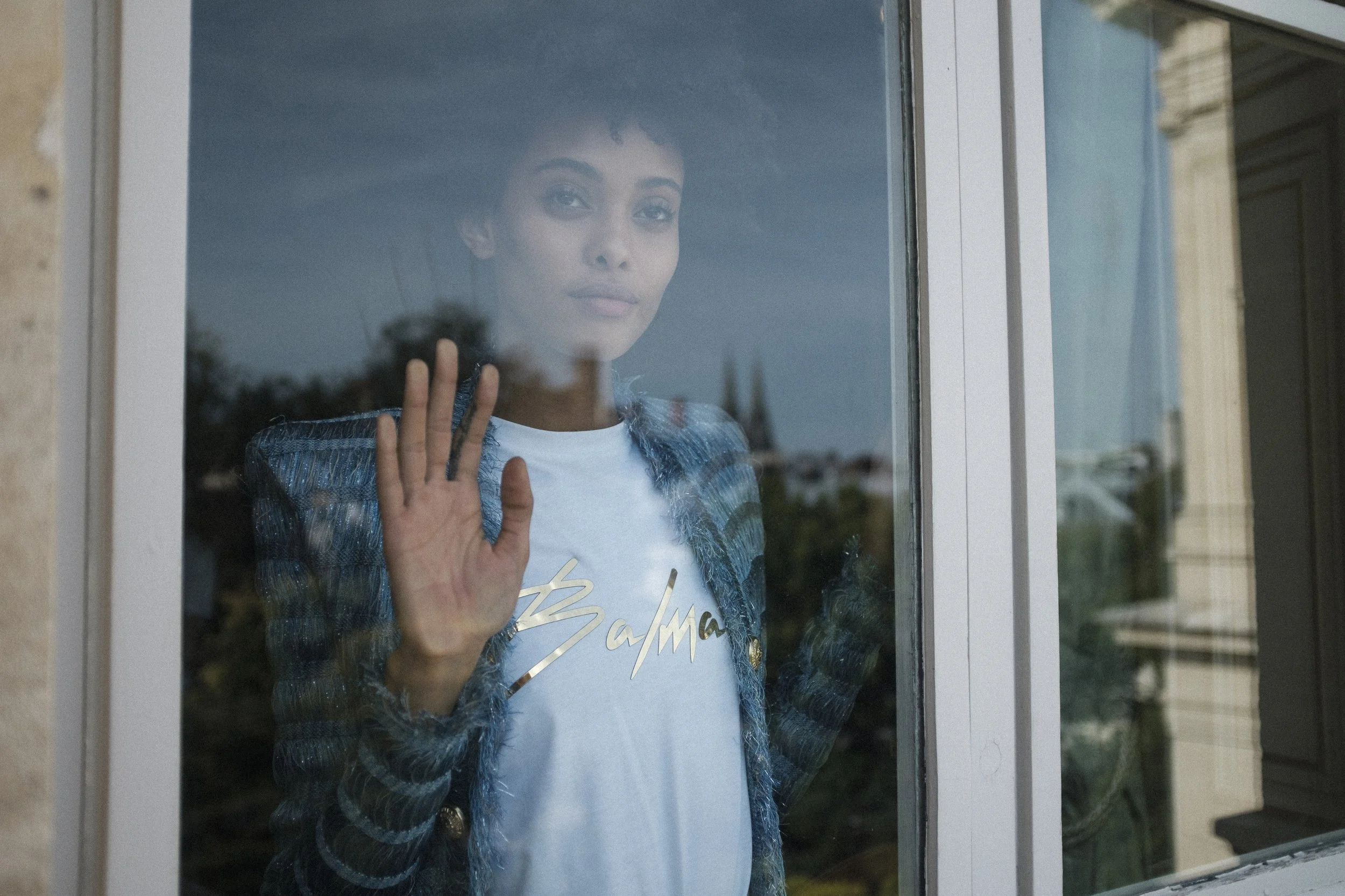 Femme regardant par une fenêtre, faisant un signe de la main.