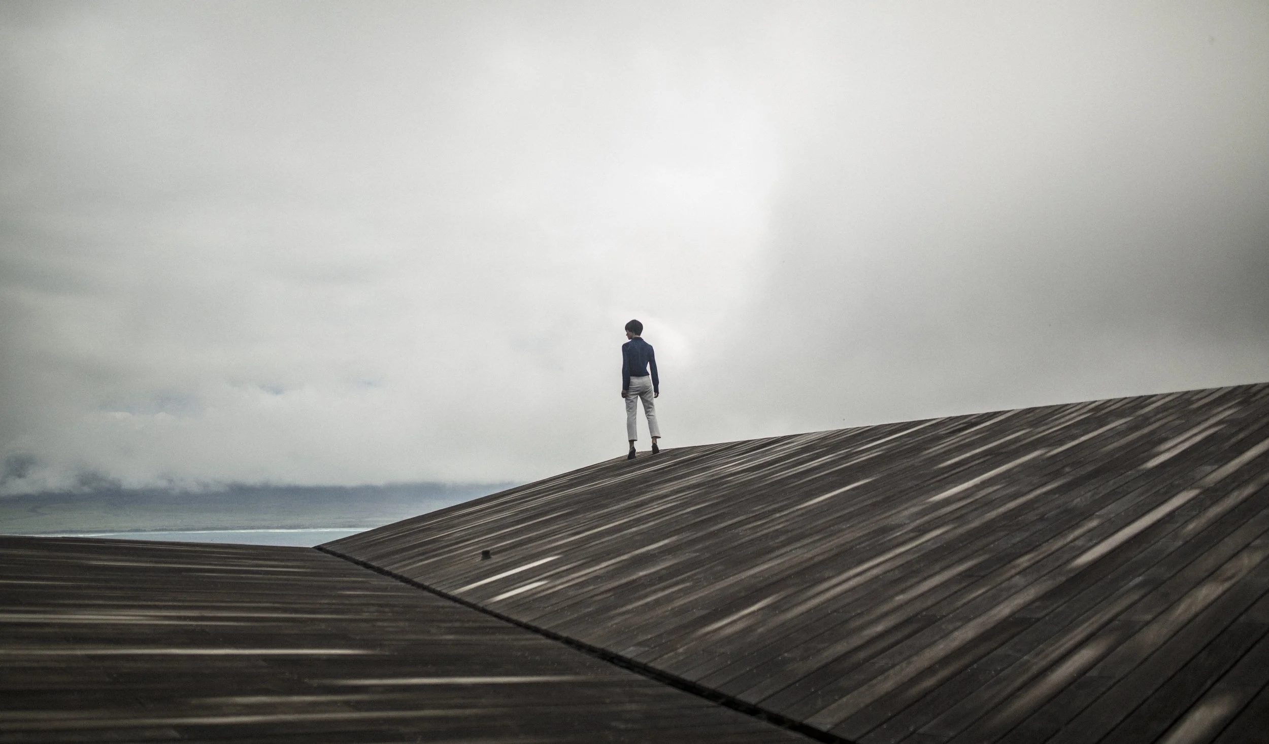 Une personne debout sur un toit en pente, regardant vers un ciel nuageux.