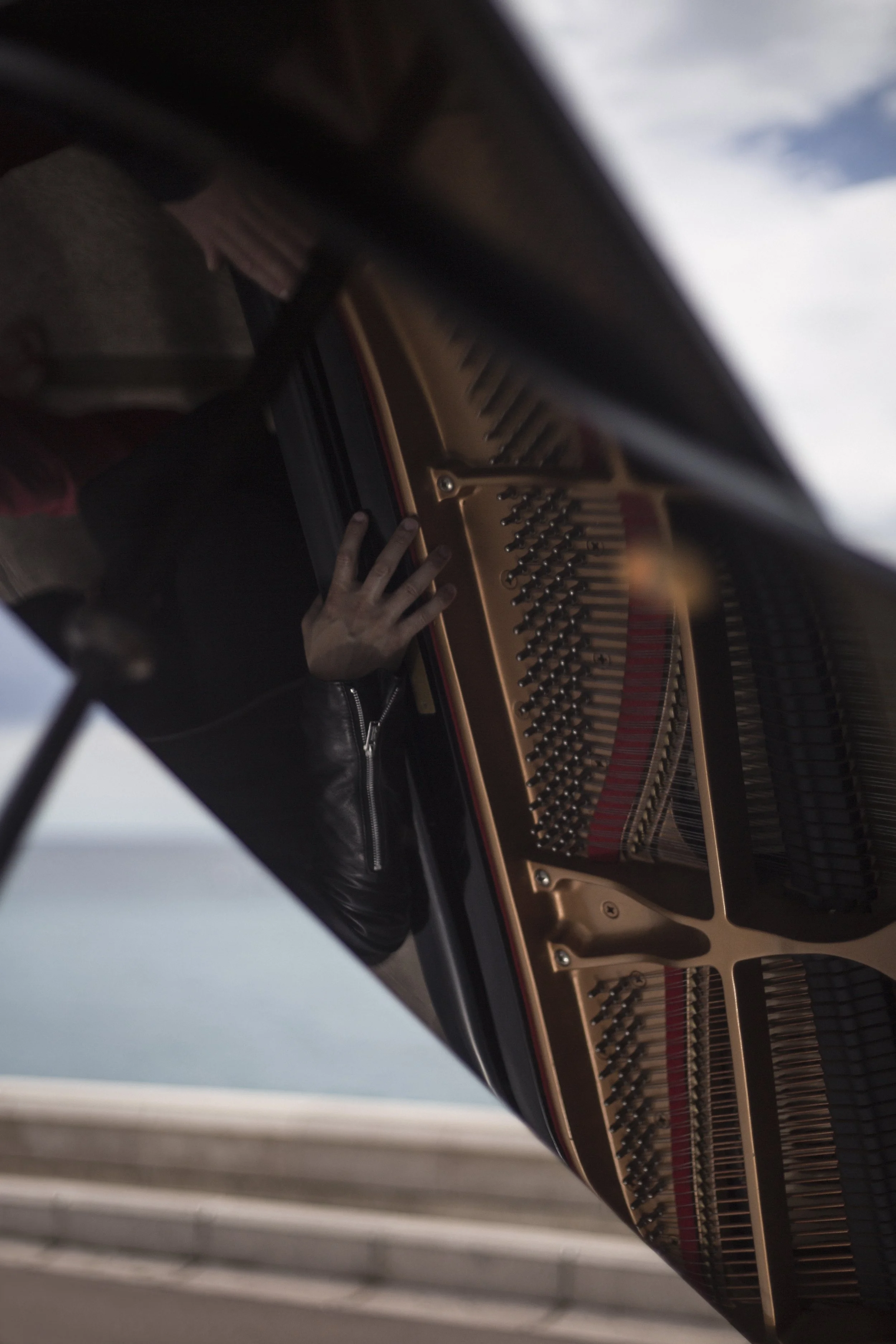 Close-up d'une personne jouant du piano à queue, vue depuis l'intérieur du piano, avec le ciel en arrière-plan.