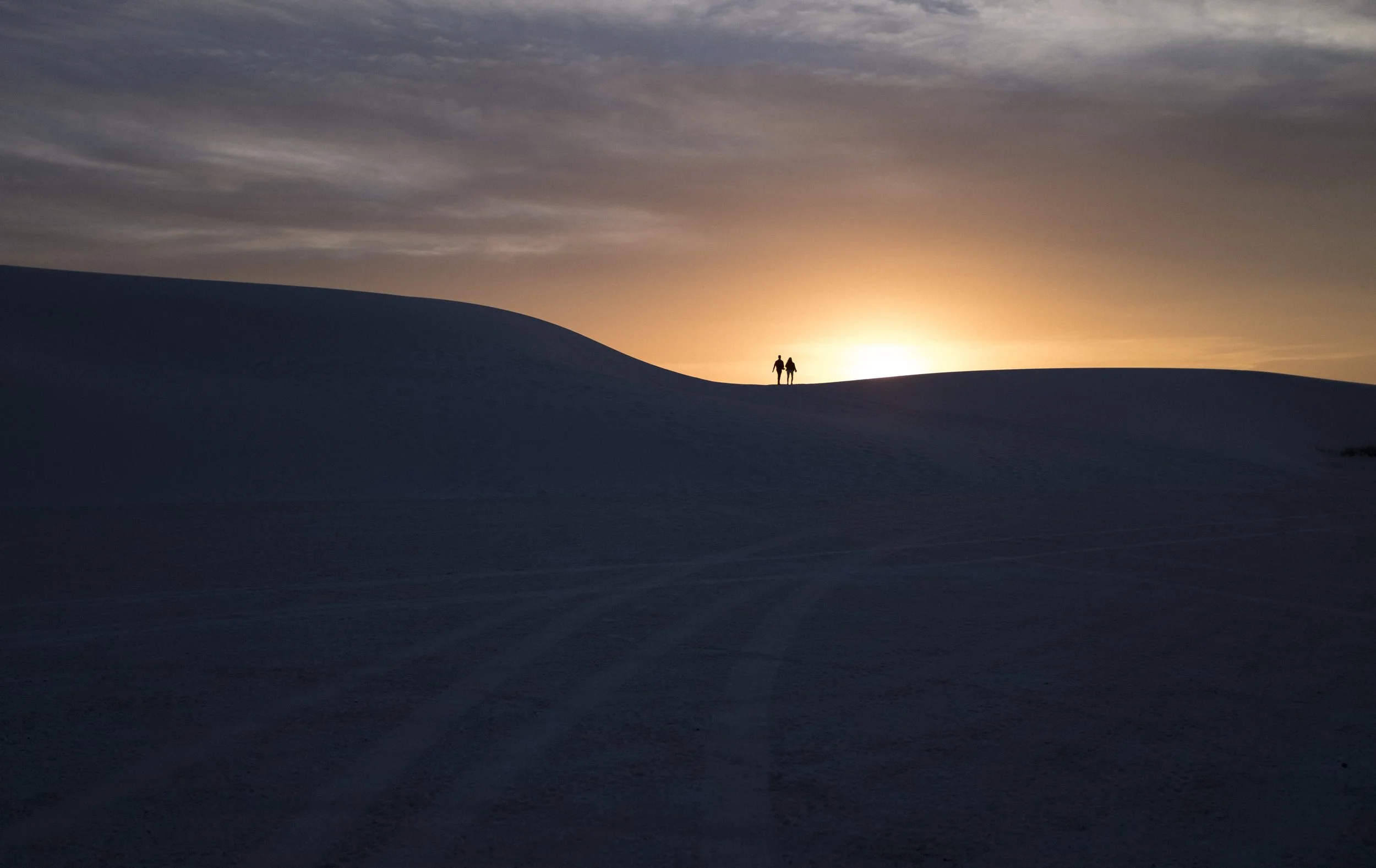 Deux personnes marchant sur une dune de sable lors d'un coucher de soleil ou d'un lever de soleil.