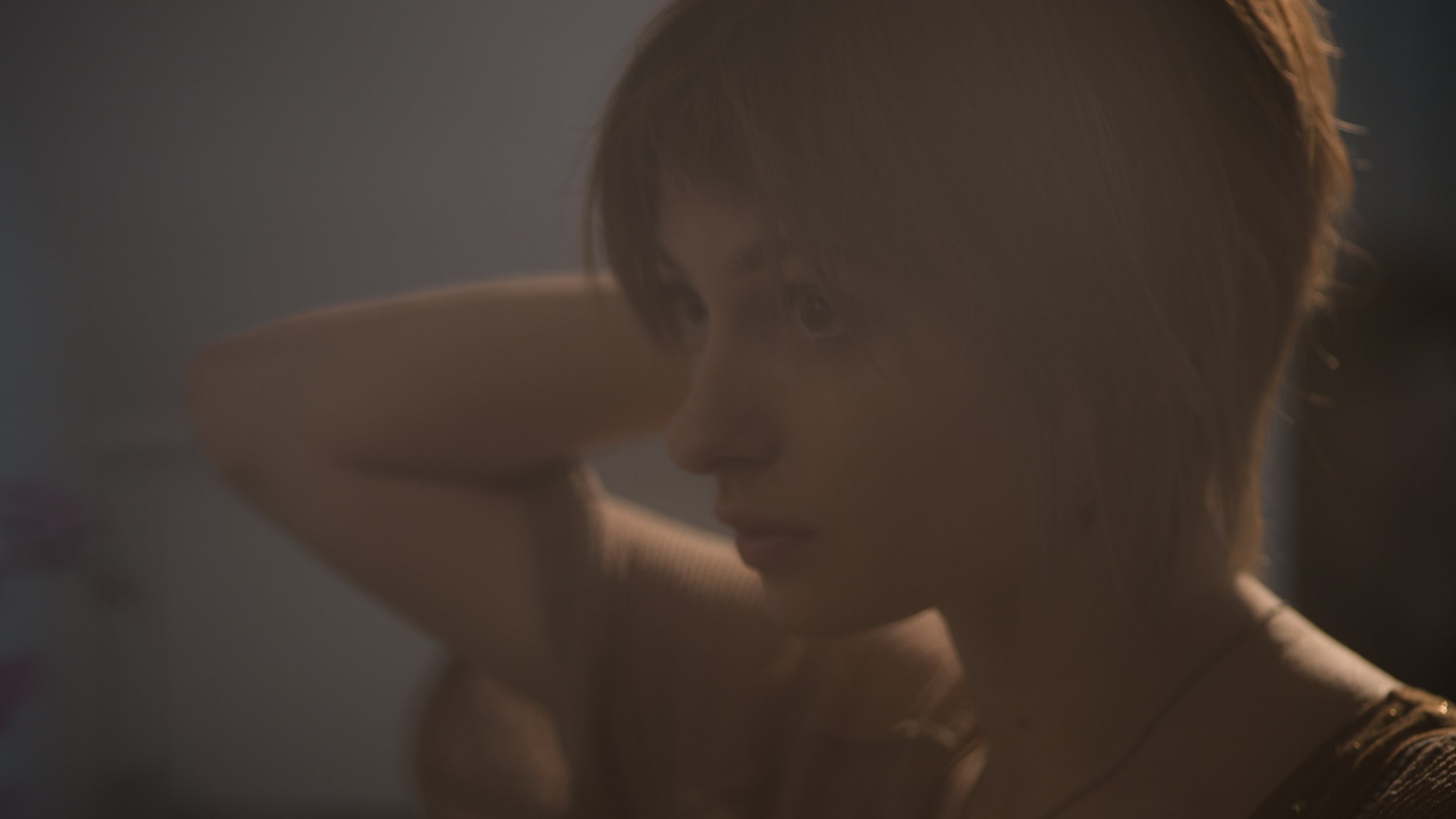 Femme aux cheveux courts, vue de profil, en train de se coiffer, dans une pièce avec un éclairage doux.