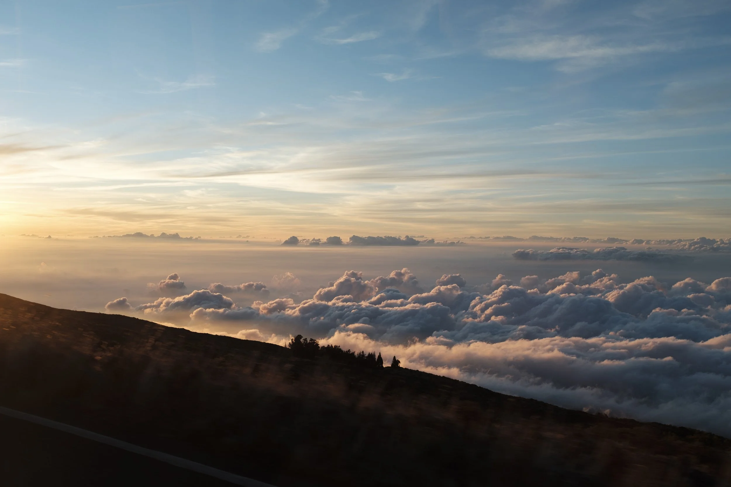 Coucher de soleil sur des nuages au-dessus d'une montagne, avec un ciel bleu et des rayons de soleil.