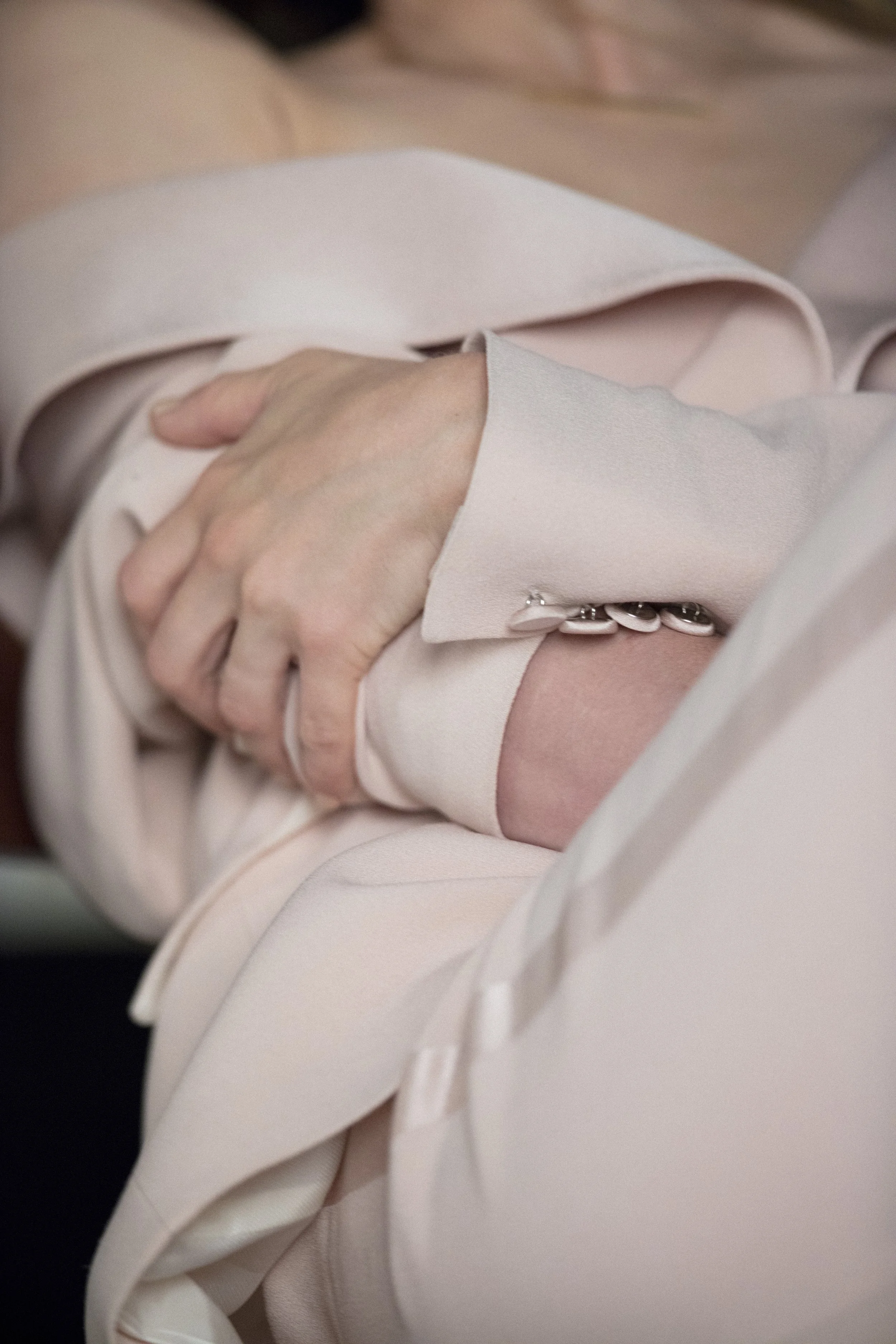 Une main tenant un vêtement de couleur pastel, probablement une personne portant une veste ou un manteau de couleur claire.