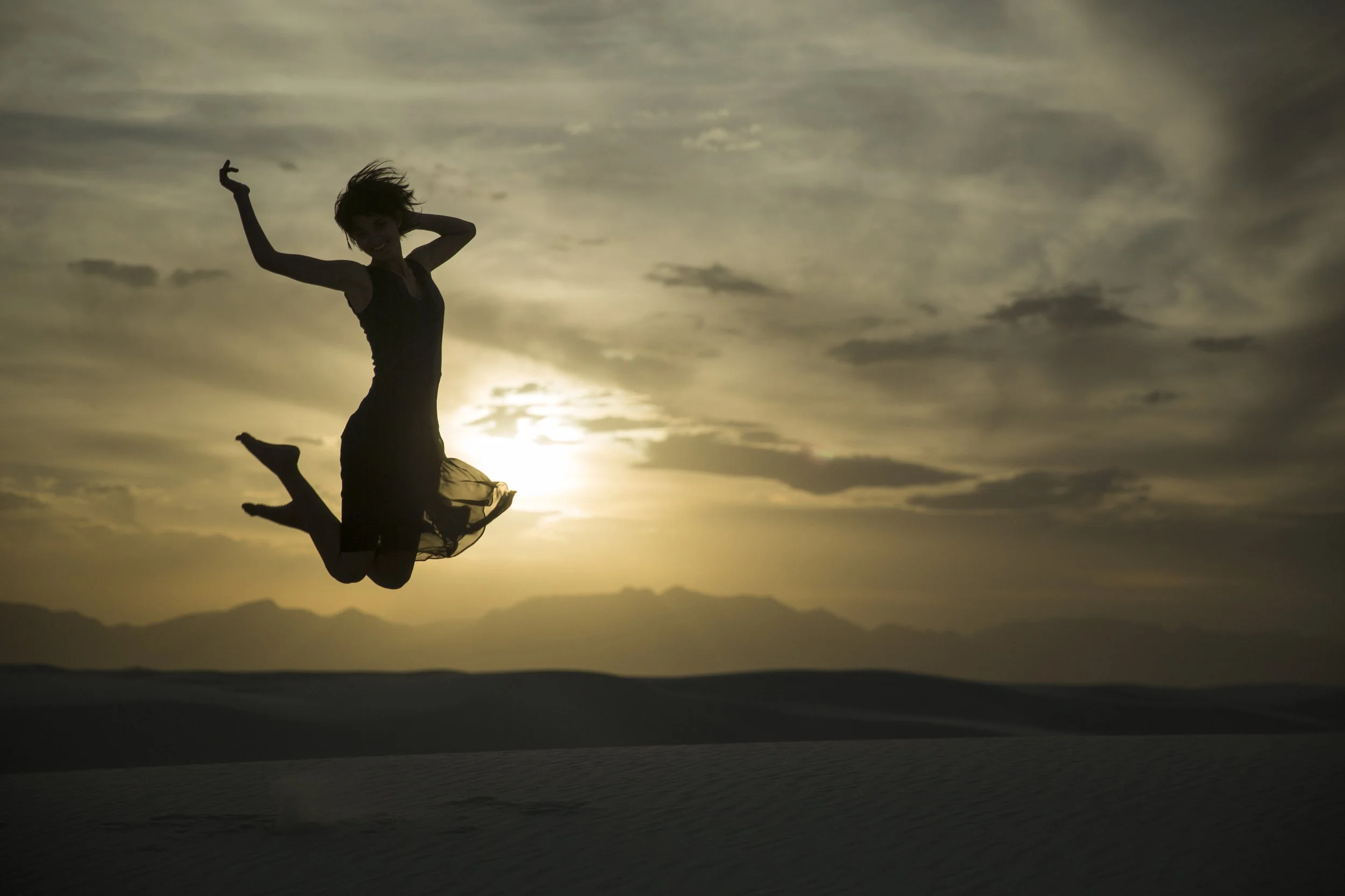 Silhouette d'une femme sautant dans un désert avec un coucher de soleil en fond.