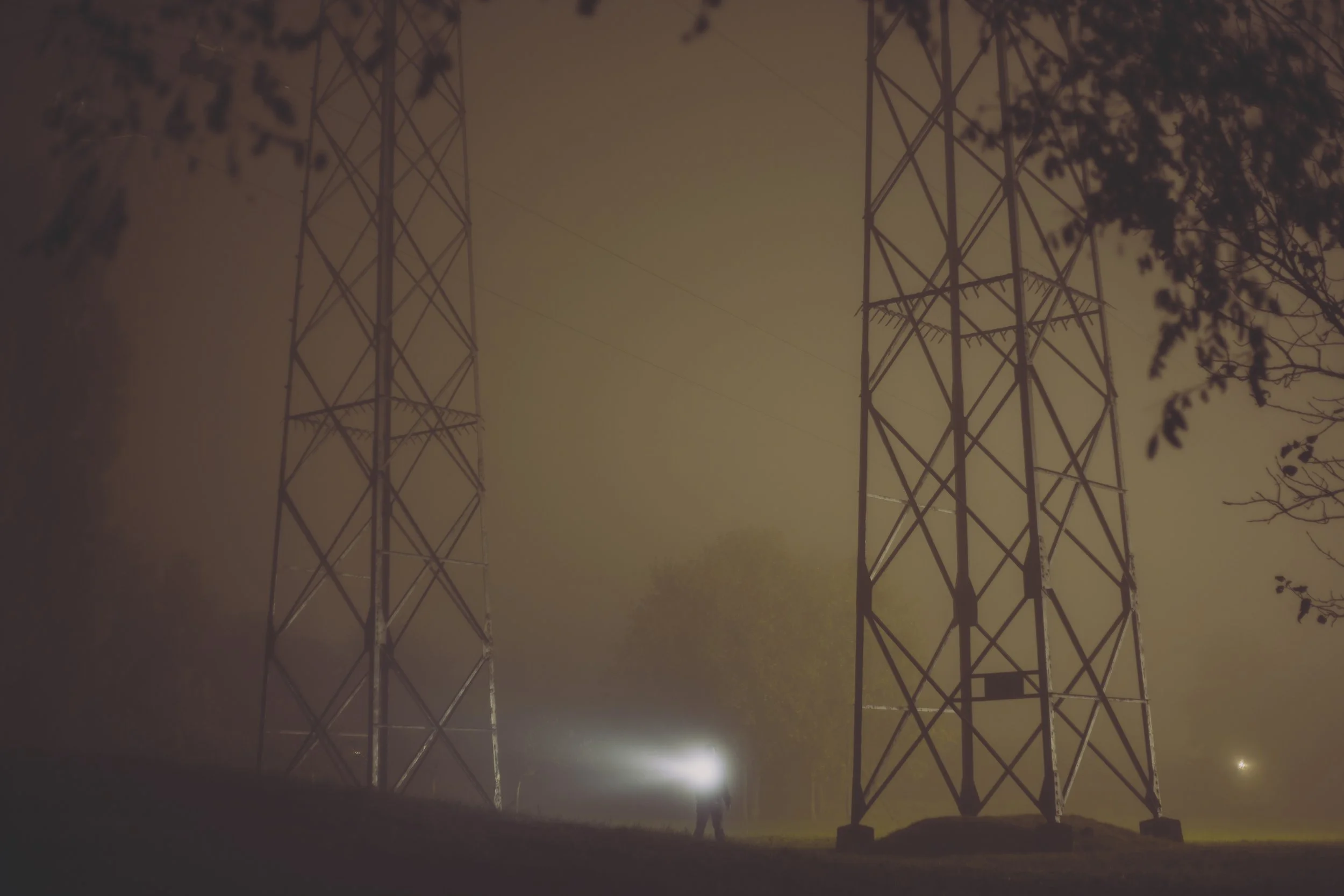 Deux pylônes électriques en acier métallique dans une brume nocturne, entourés d'arbres.
