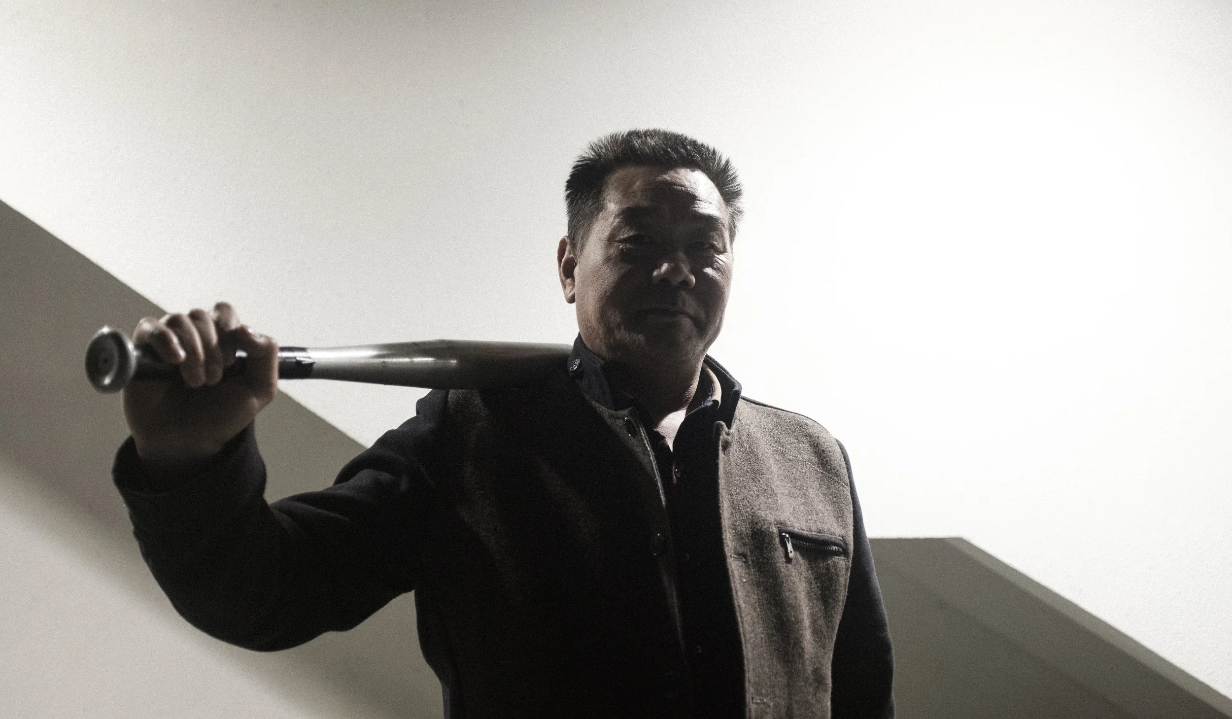 Homme avec un gant de baseball sur l'épaule, utilisant un éclairage faible qui crée une silhouette, dans un intérieur à plafond blanc.