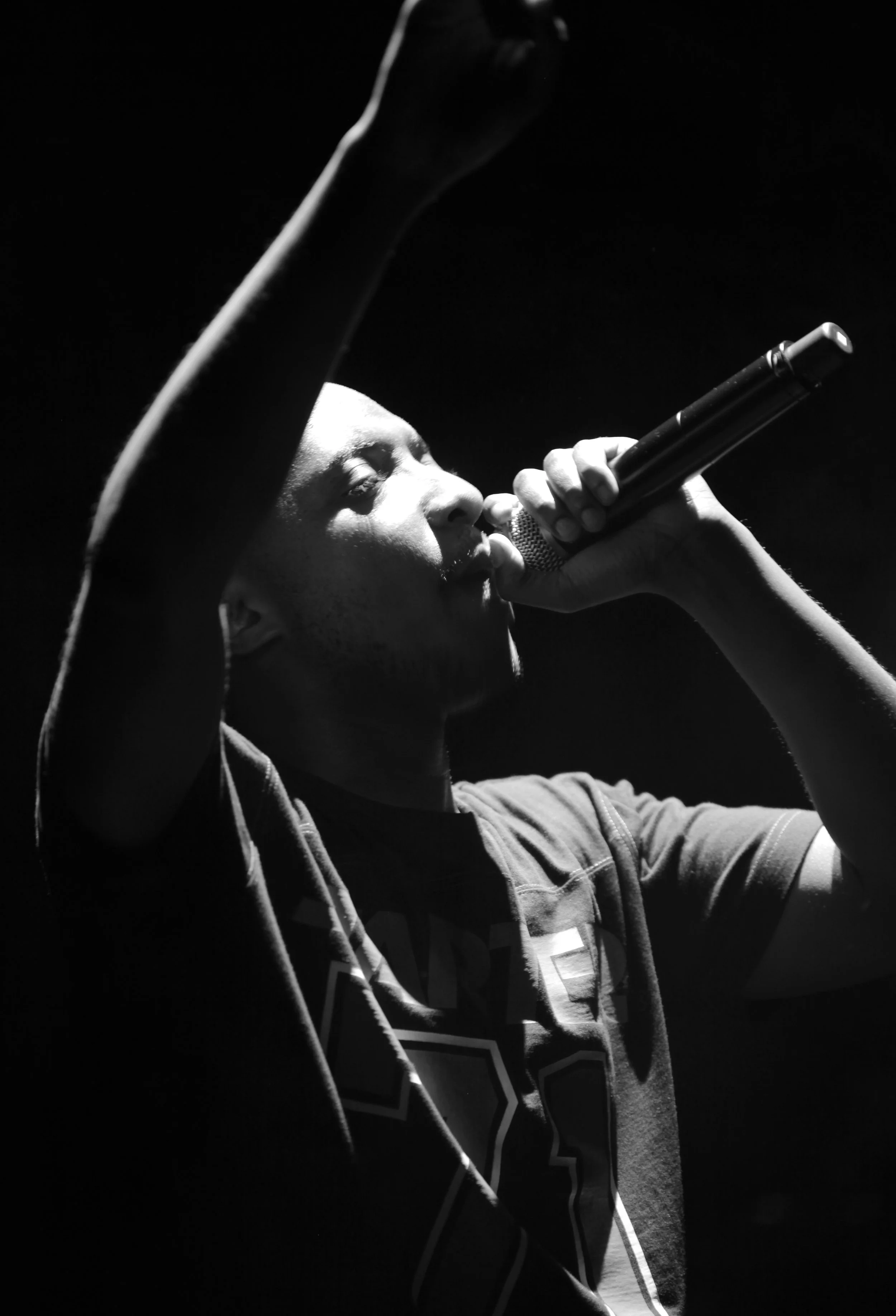 Homme noirchant dans un microphone, en noir et blanc, avec un bras levé.