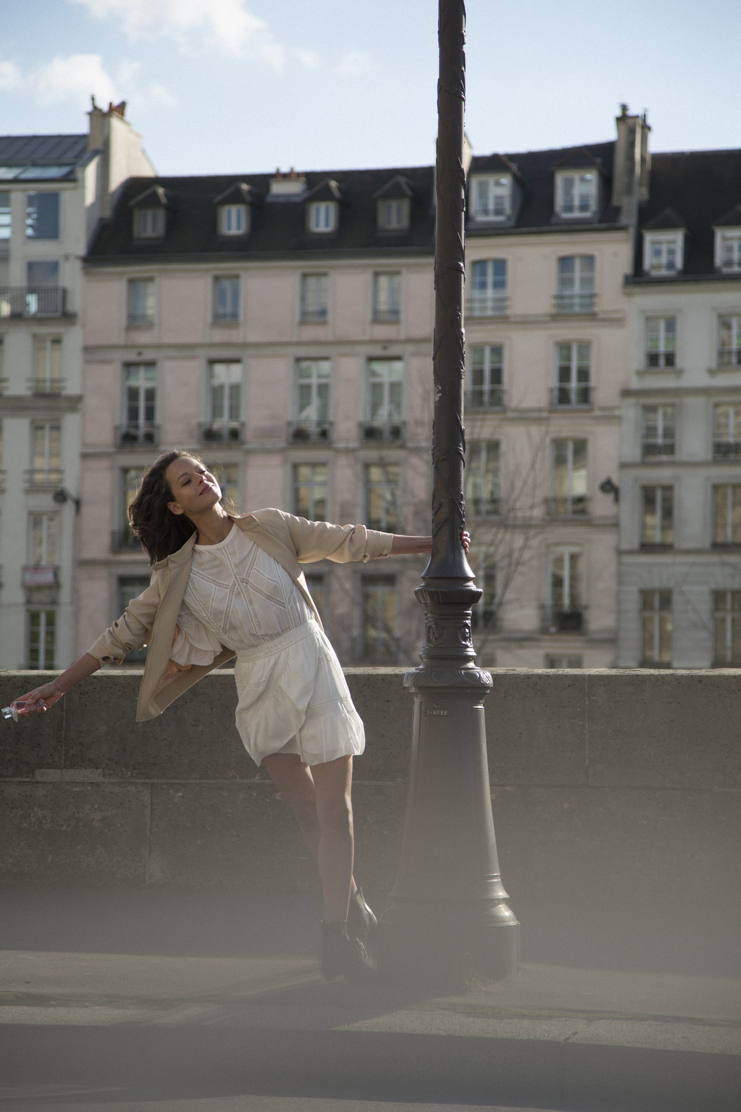 Jeune femme posant à côté d'un lampadaire en extérieur avec bâtiments résidentiels en arrière-plan.