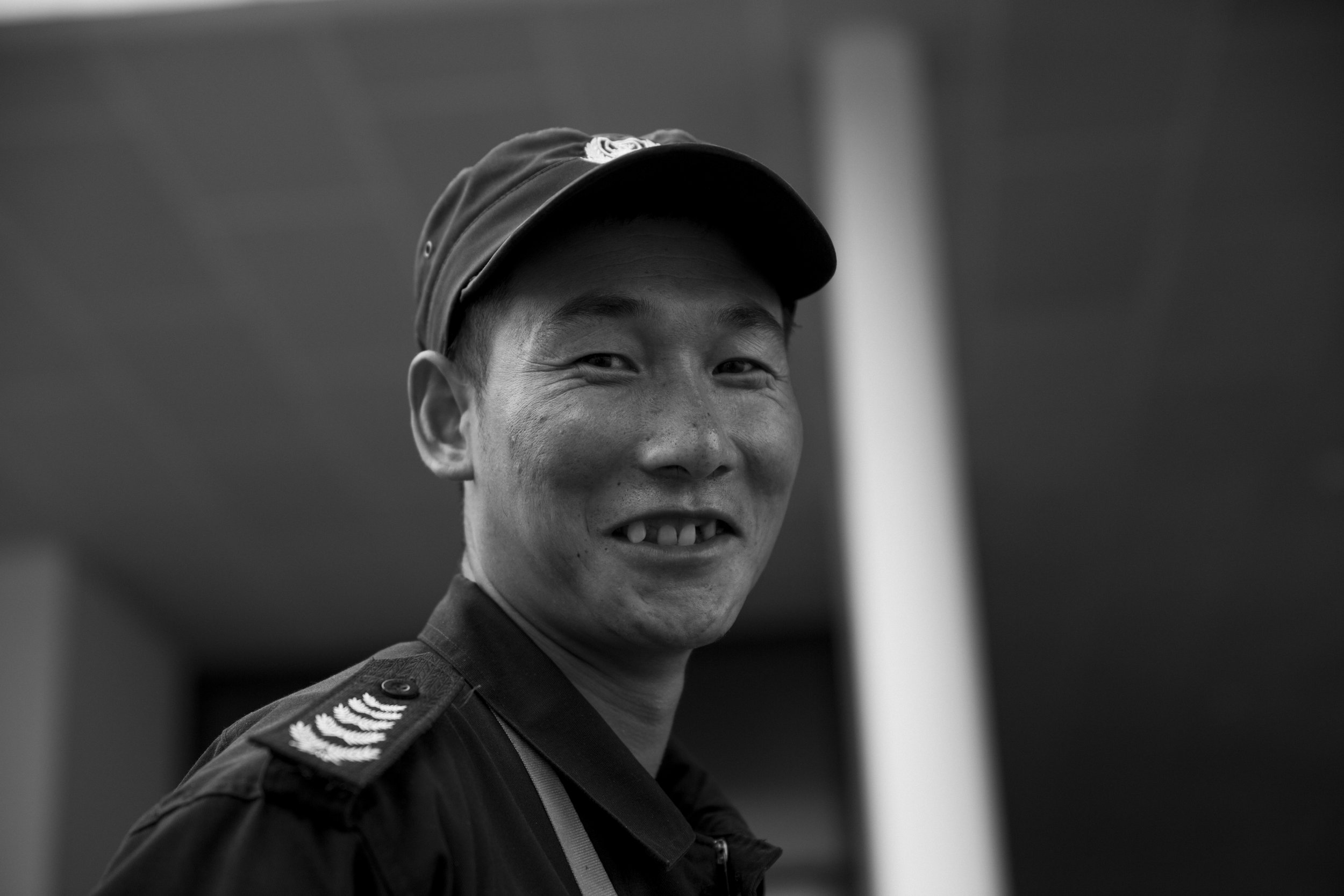 Portrait noir et blanc d'un homme militaire souriant, portant une casquette et un uniforme, avec une coiffure courte.