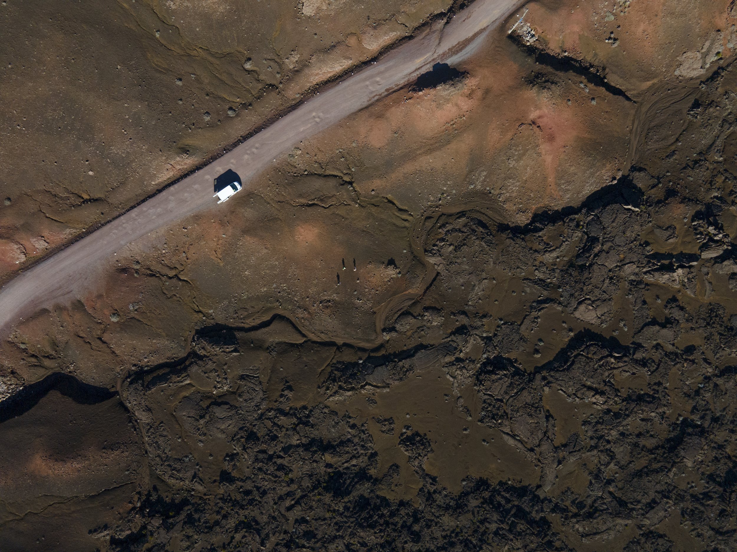 Une vue aérienne d'une route en terre dans un paysage désertique avec des formations rocheuses et trois personnes marchant le long de la route.