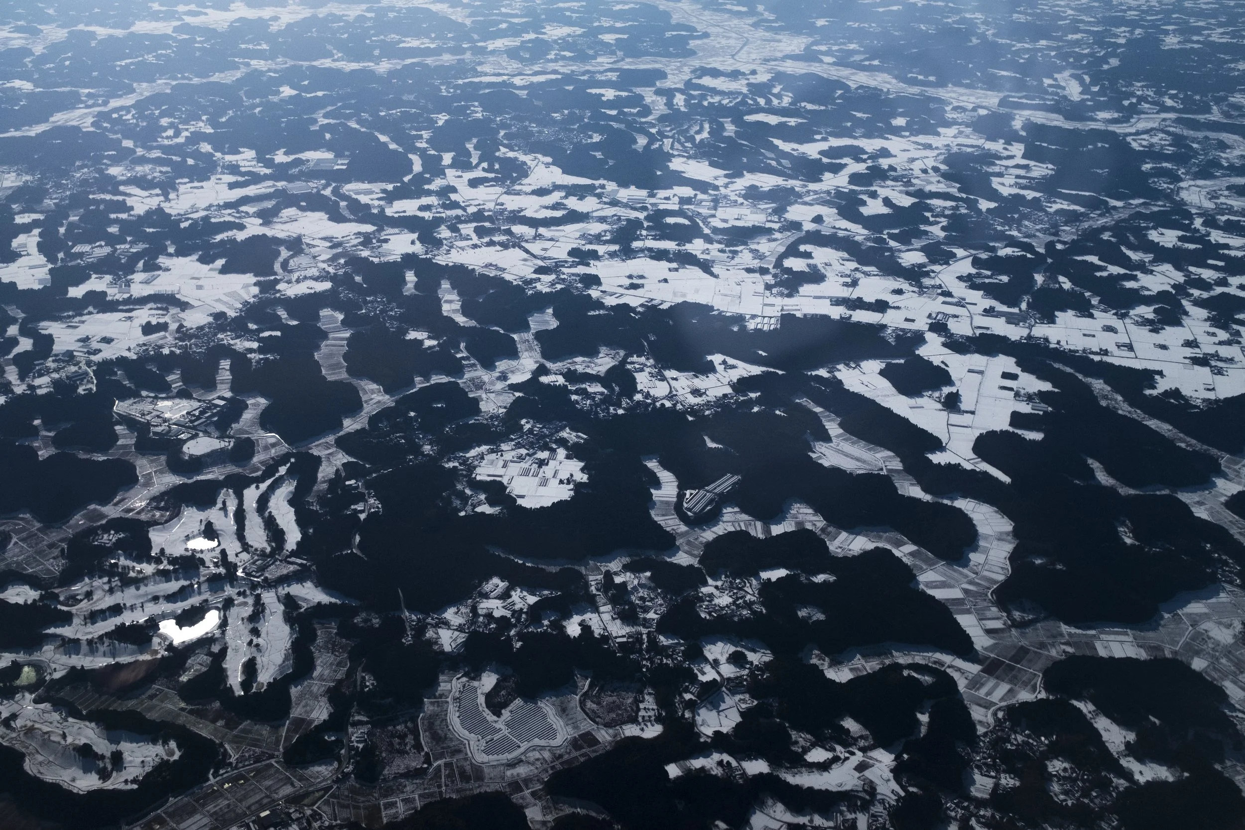 Vues aériennes d'un paysage enneigé avec des champs agricoles, des forêts et des plans d'eau, sous un ciel clair.