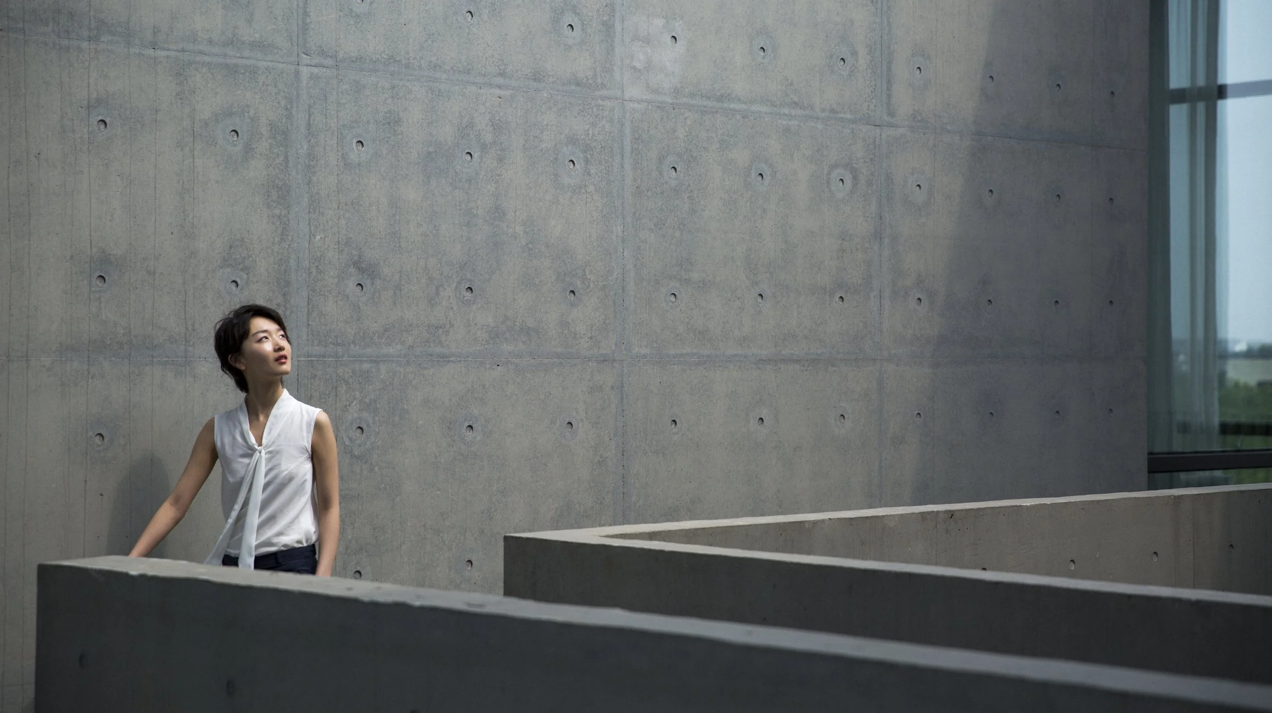 Jeune femme tenant la main courante dans un bâtiment moderne avec mur en béton et grande fenêtre en arrière-plan.