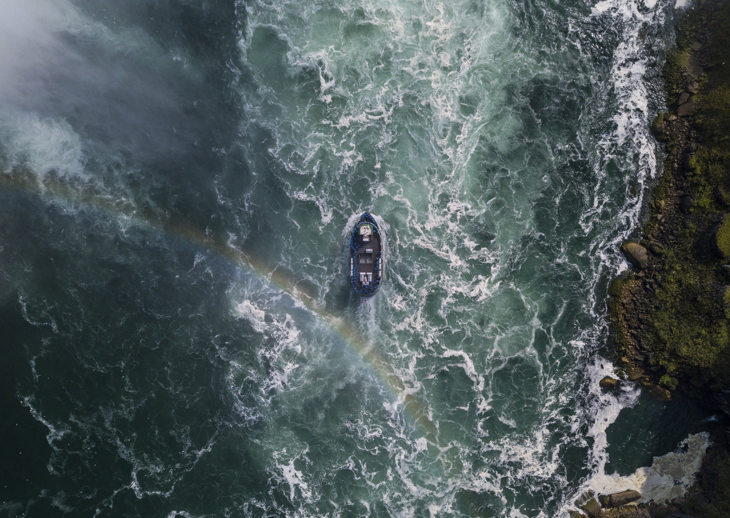 Vue aérienne d'une embarcation naviguant dans une rivière à écoulement rapide, entourée de rochers et de végétation.